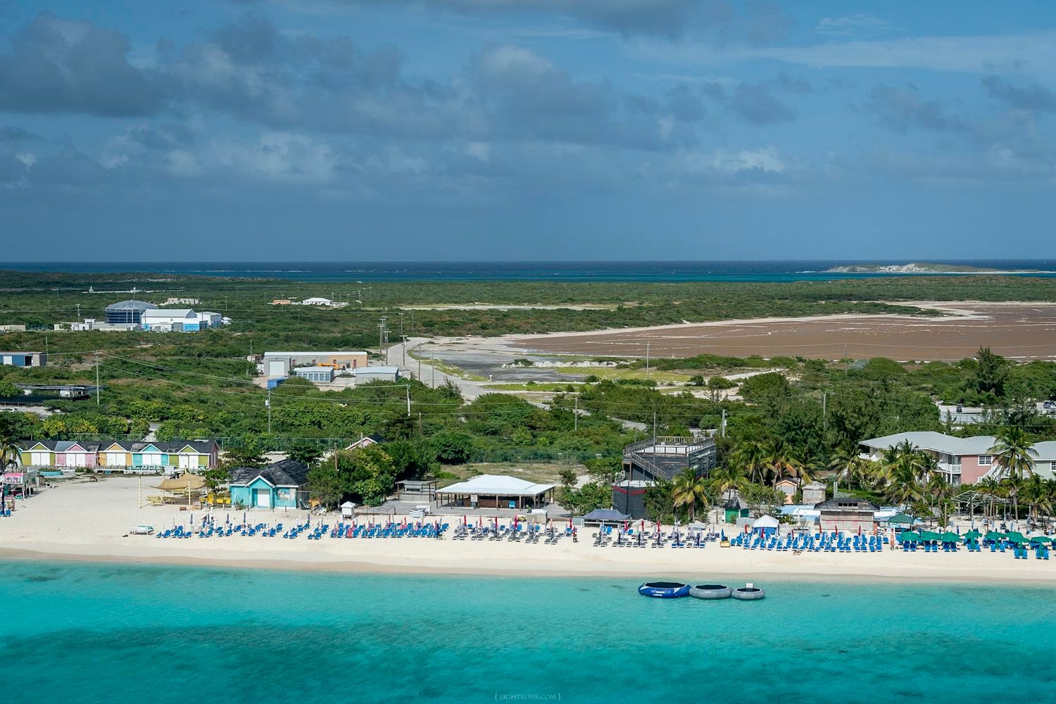 Aerial view of a tropical beach resort with turquoise waters, white sand, and colorful beach chairs in the Caribbean.