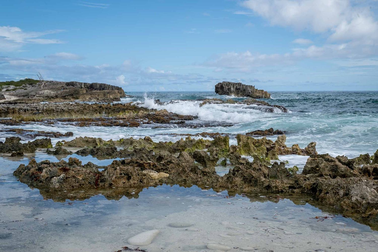 Panoramic view of rugged rocky coastline with crashing waves and blue ocean waters under bright sunny sky.