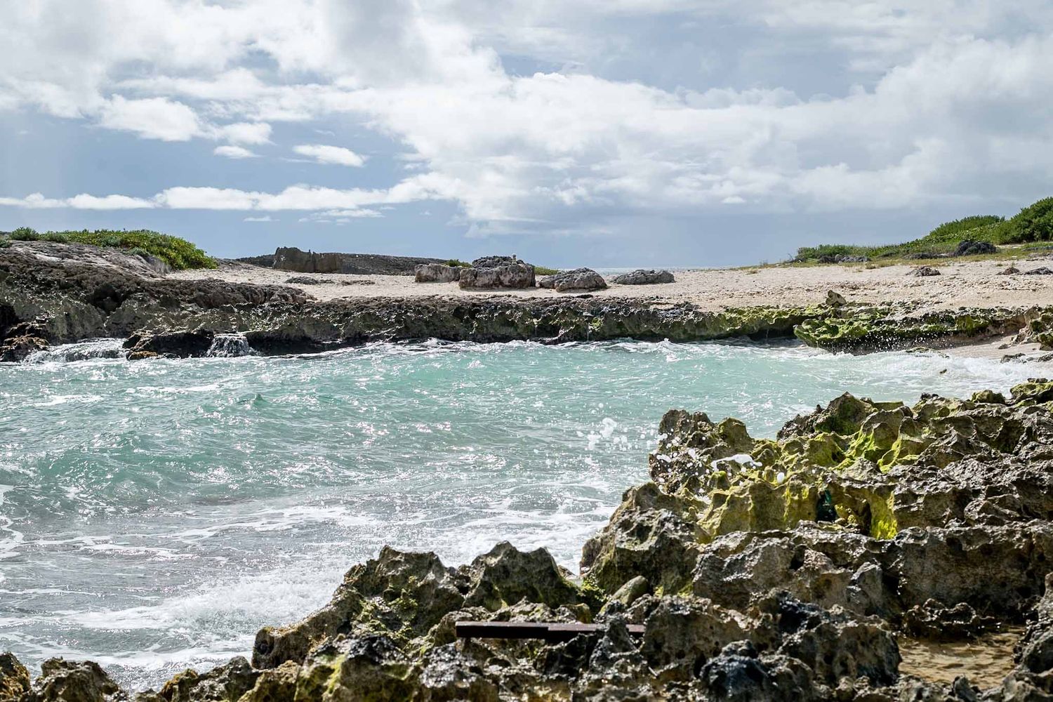 Rocky coastline with crashing waves and rugged cliffs stretching along the shoreline under cloudy skies.