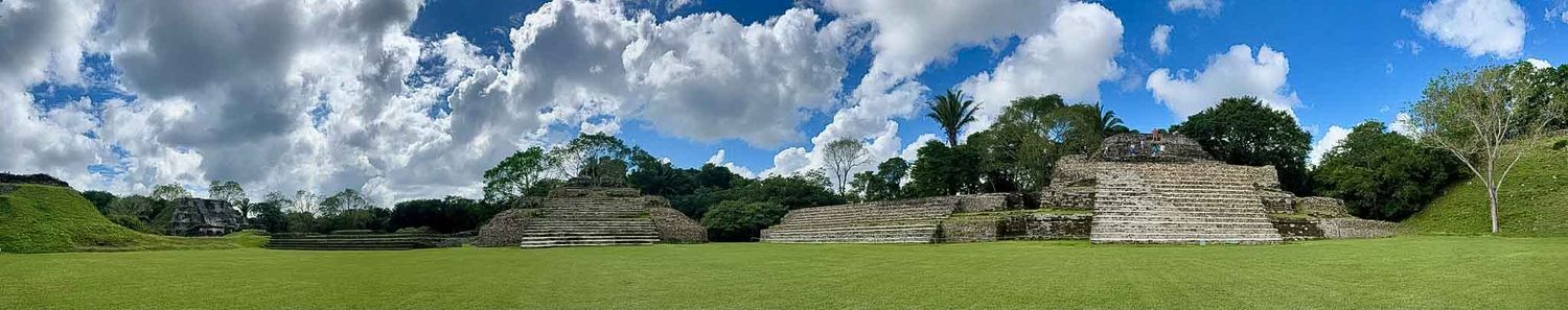 A scenic panoramic view of green rolling hills with dramatic clouds in the sky and a stone structure in the distance.