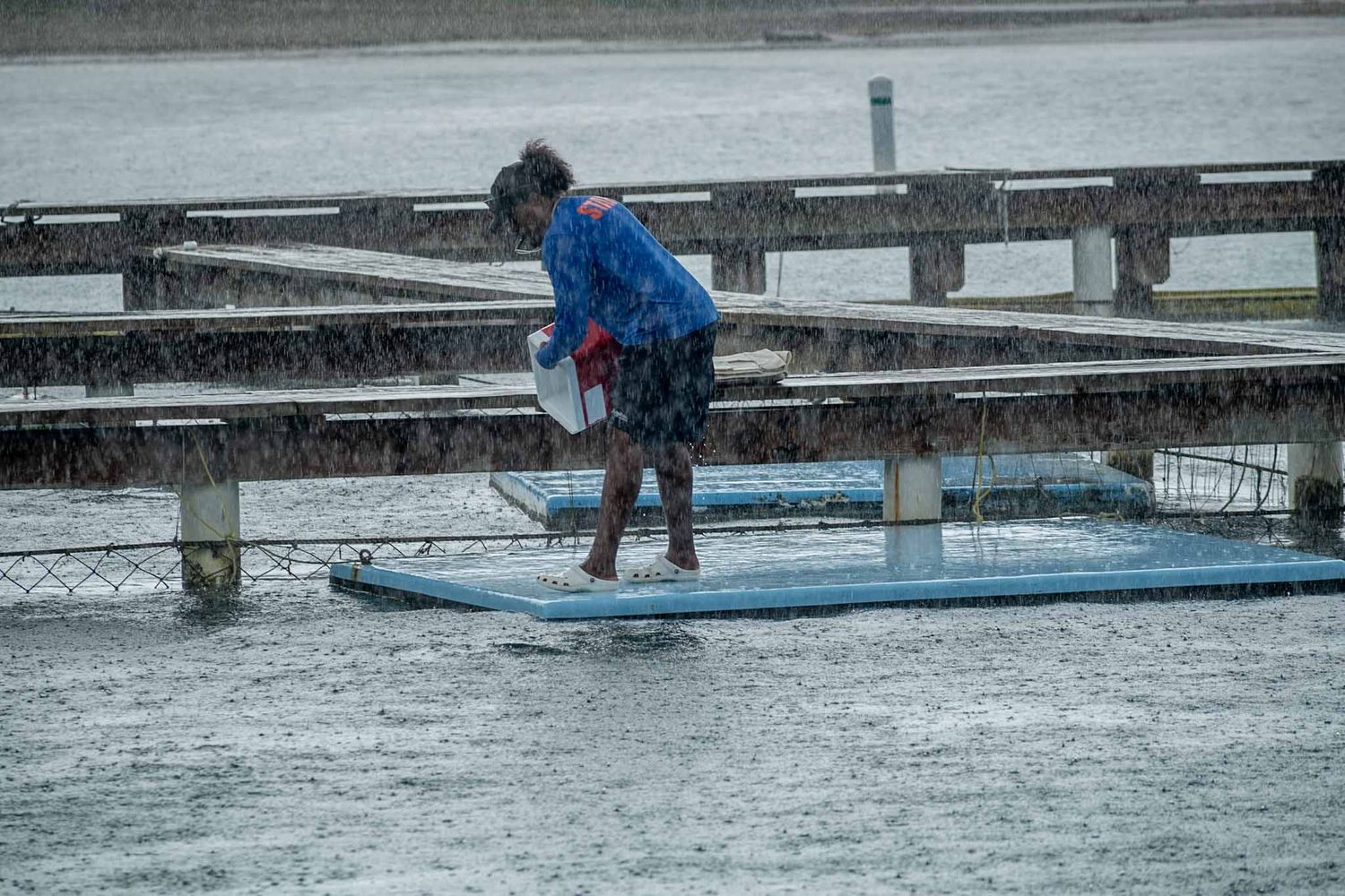 A person in blue winter gear works on maintaining a snow-covered dock at a marina during winter weather.