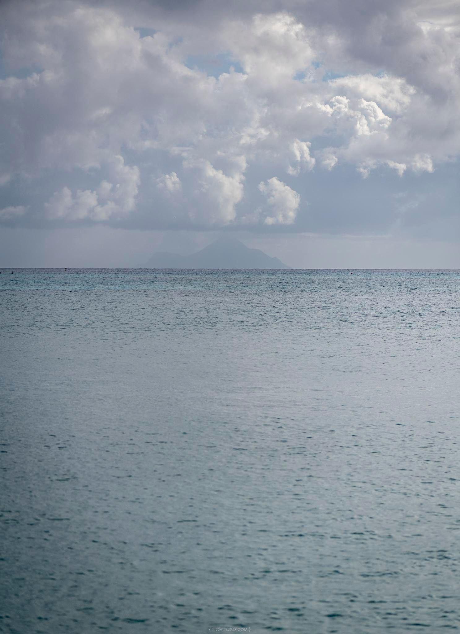 Calm blue ocean with a distant volcanic mountain silhouette under dramatic cloudy skies.