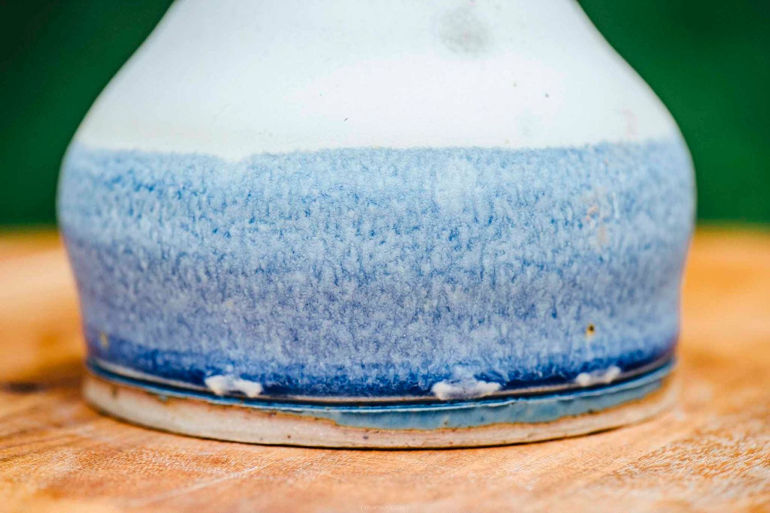 Close-up of a blue and white ceramic vase with gradient glaze texture, resting on a wooden surface.