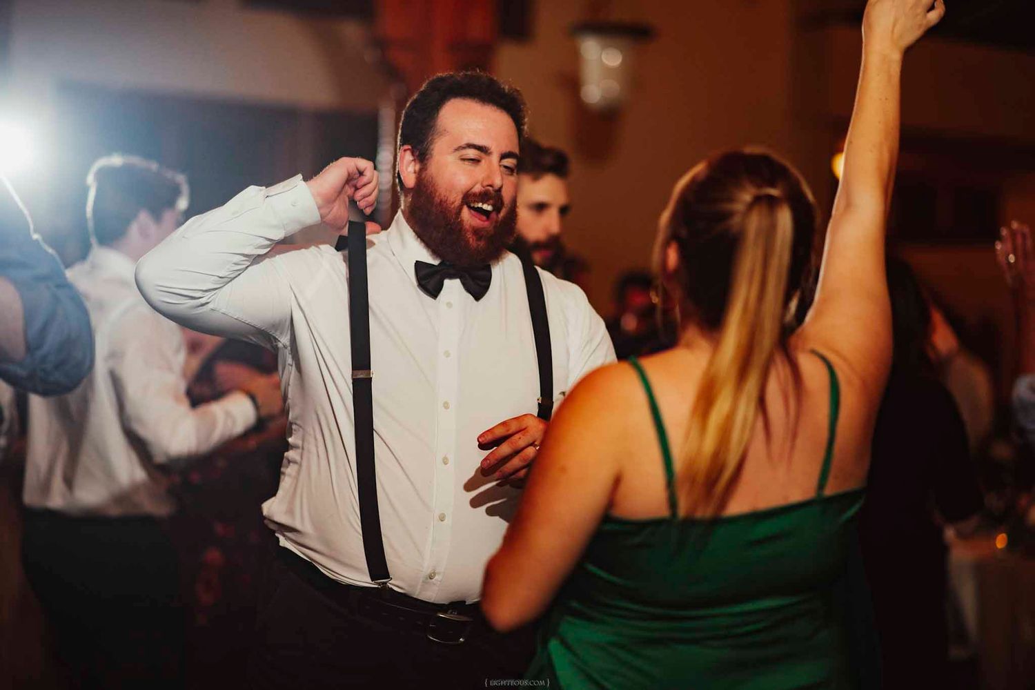 Man in suspenders and bow tie dancing energetically at a wedding reception party.