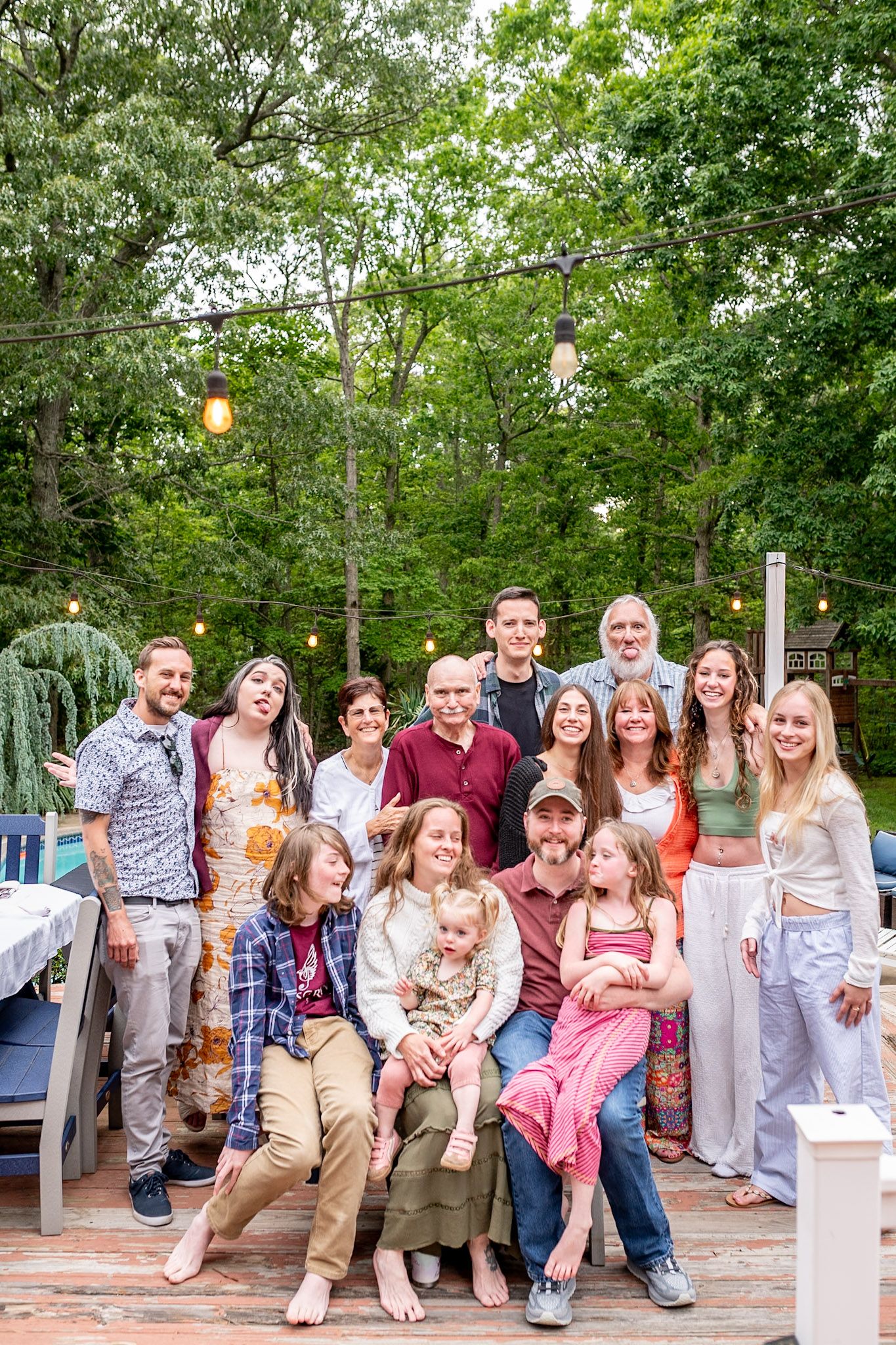 A large group poses together outdoors at a casual gathering on a patio surrounded by greenery.