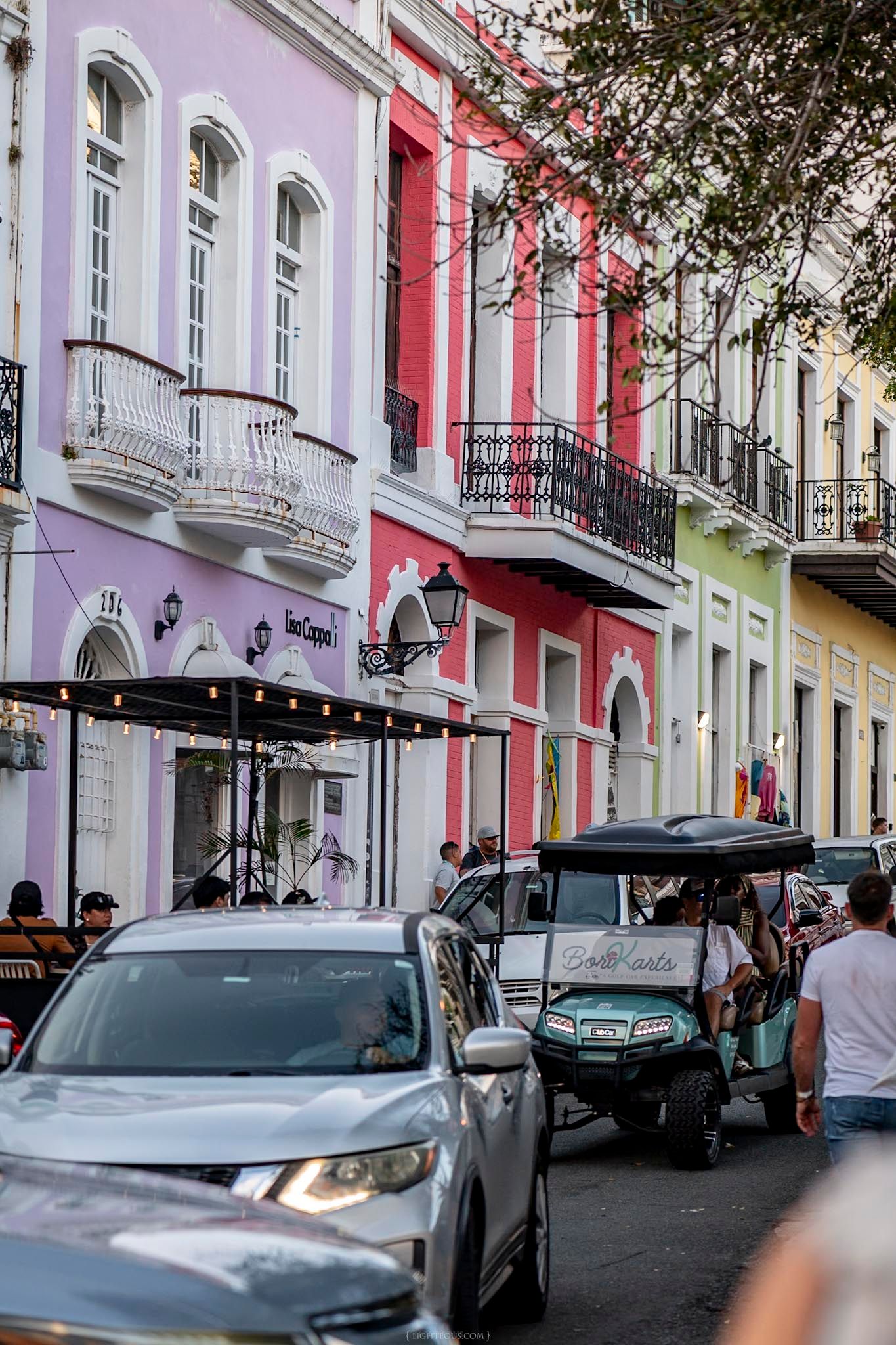 Colorful colonial buildings line a busy street in Old San Juan, Puerto Rico, with a golf cart and cars passing by.