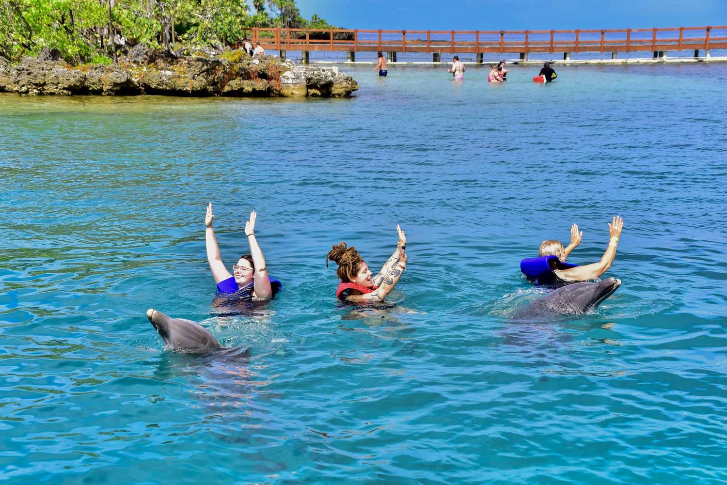 People floating and swimming in crystal clear turquoise waters near a rocky coastline on a sunny day.