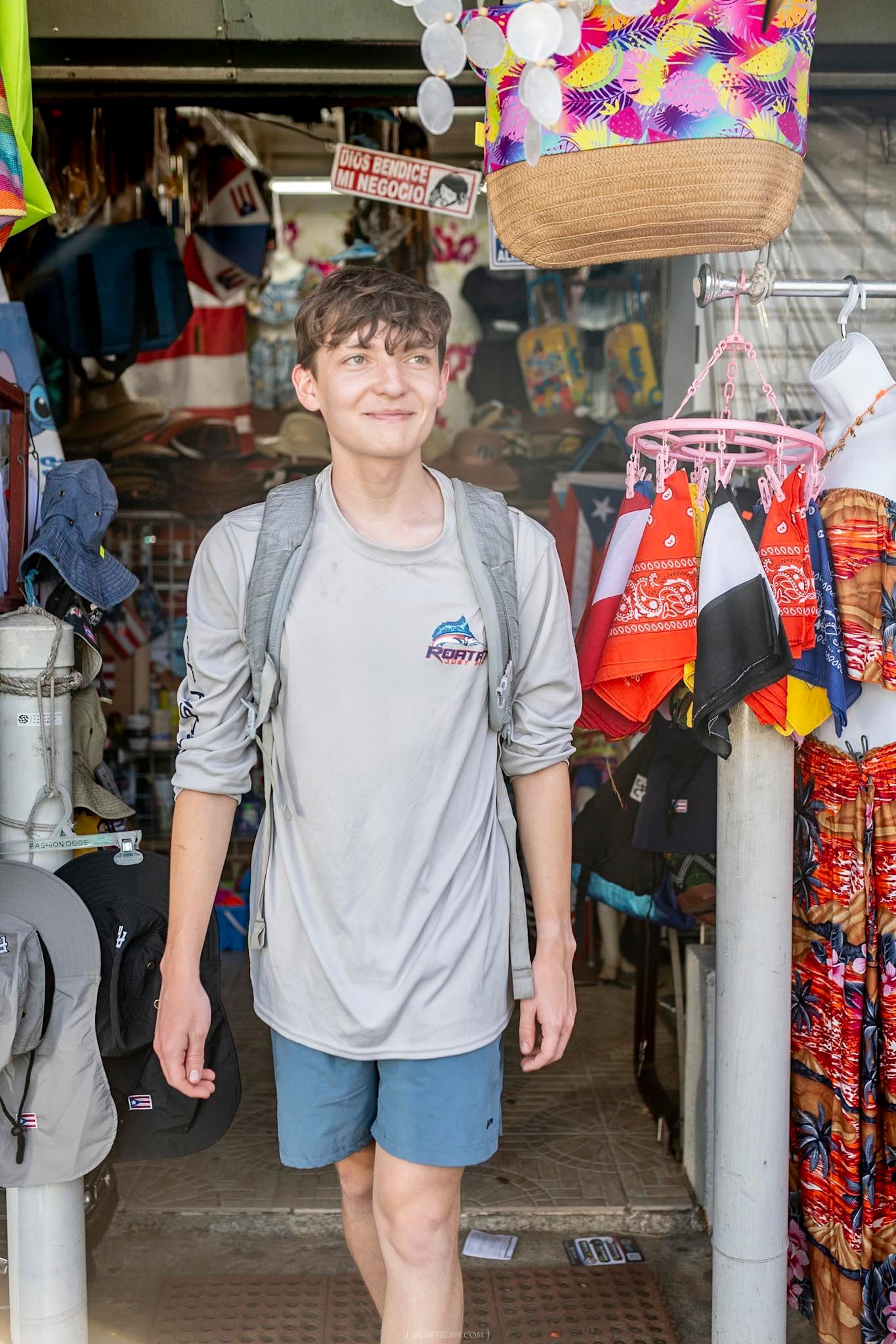 Young man with backpack smiling while standing in the entrance of a colorful souvenir shop.