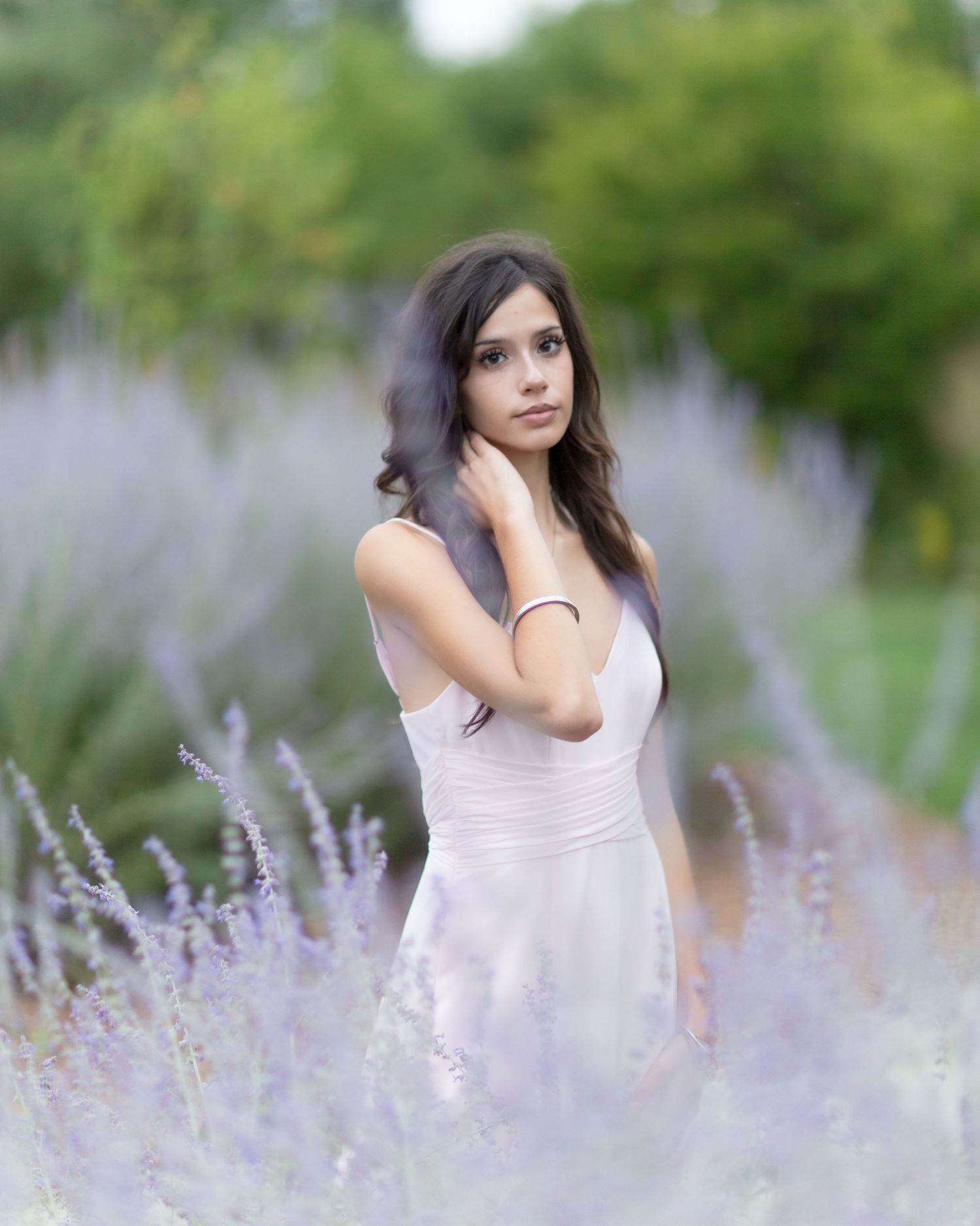 Young woman in white dress standing among purple lavender flowers in a garden, soft bokeh background.