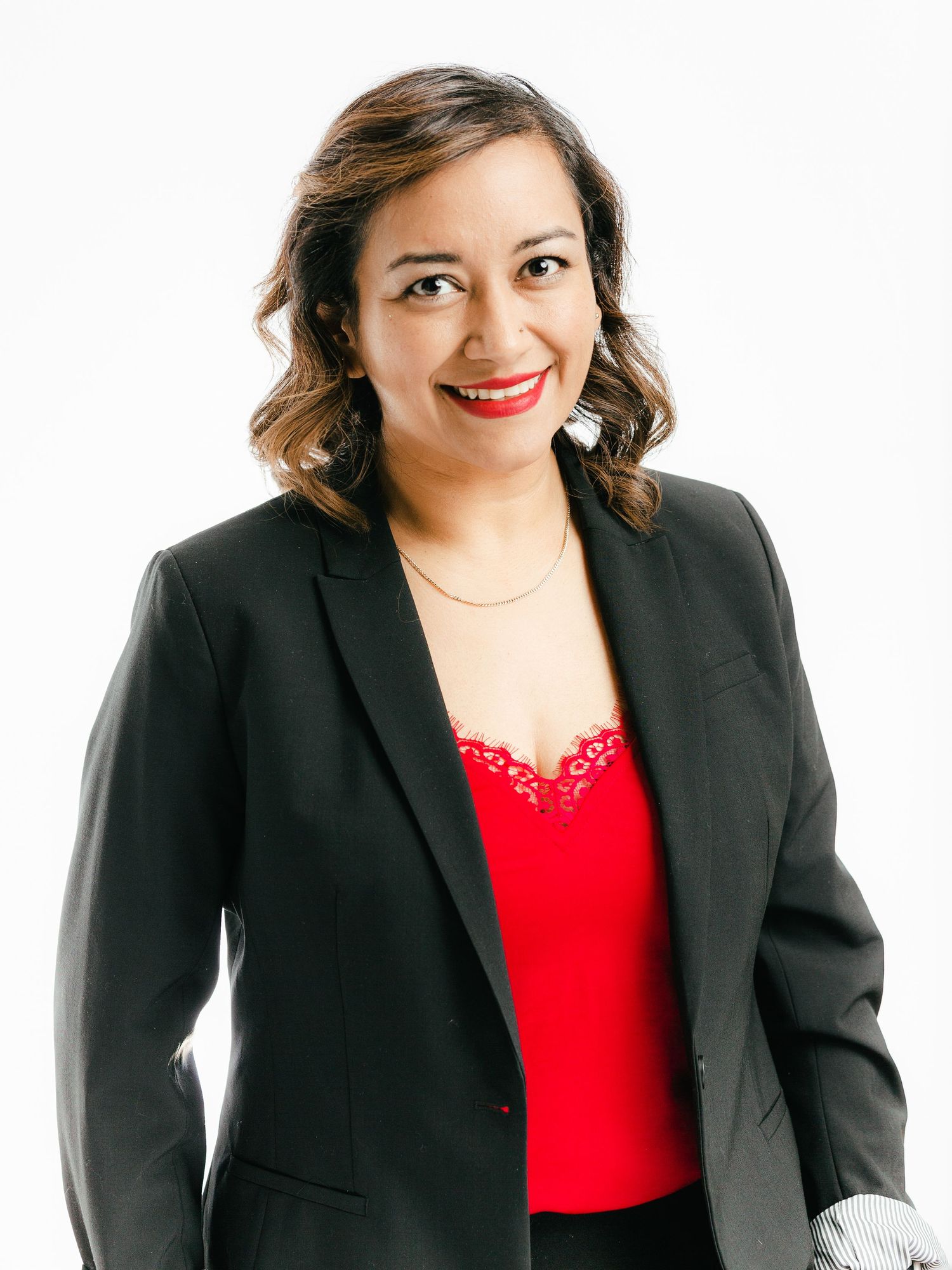 Smiling woman in red top and black blazer posing against a white background professional portrait.
