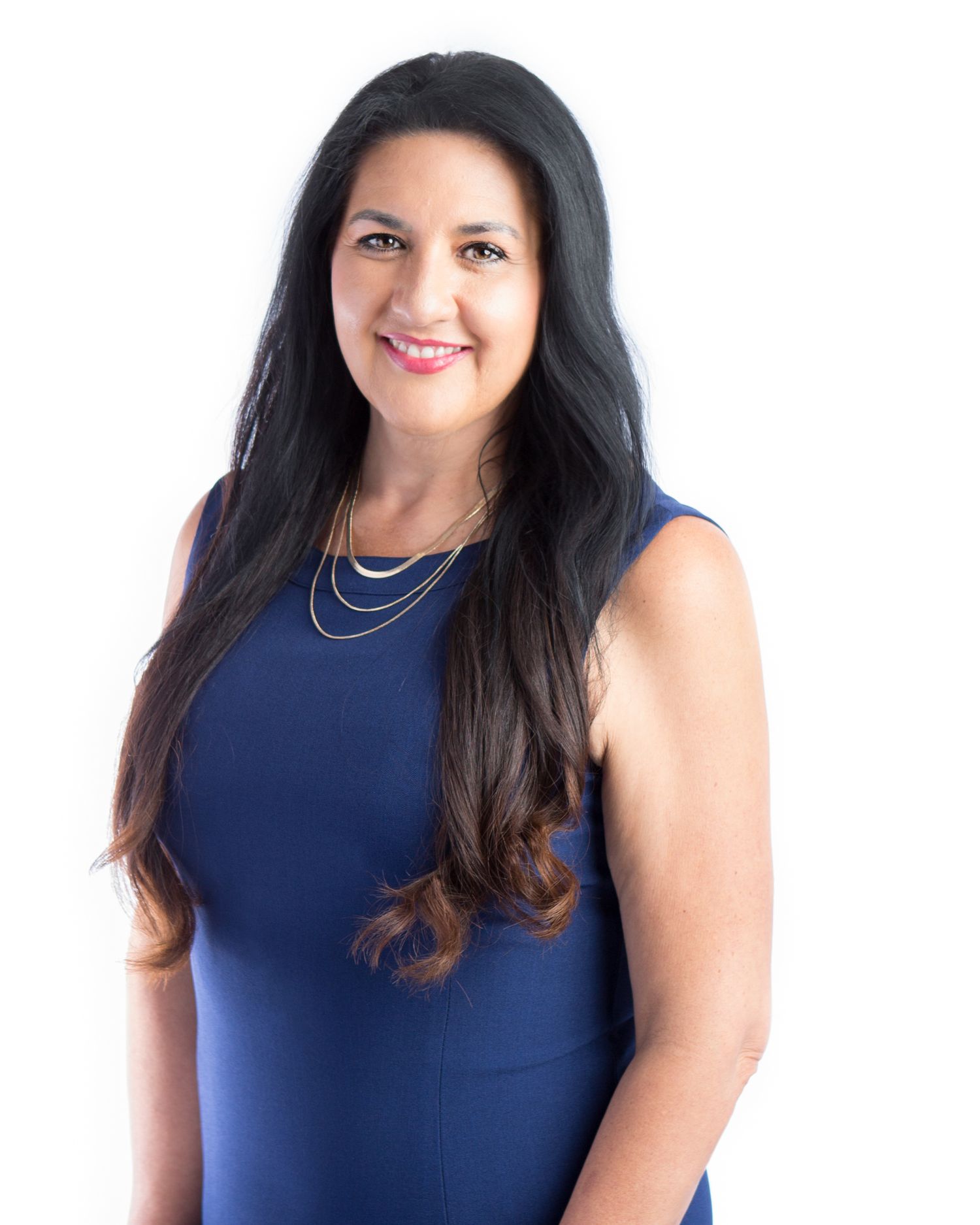 Professional woman in blue sleeveless dress with layered necklaces smiling confidently.