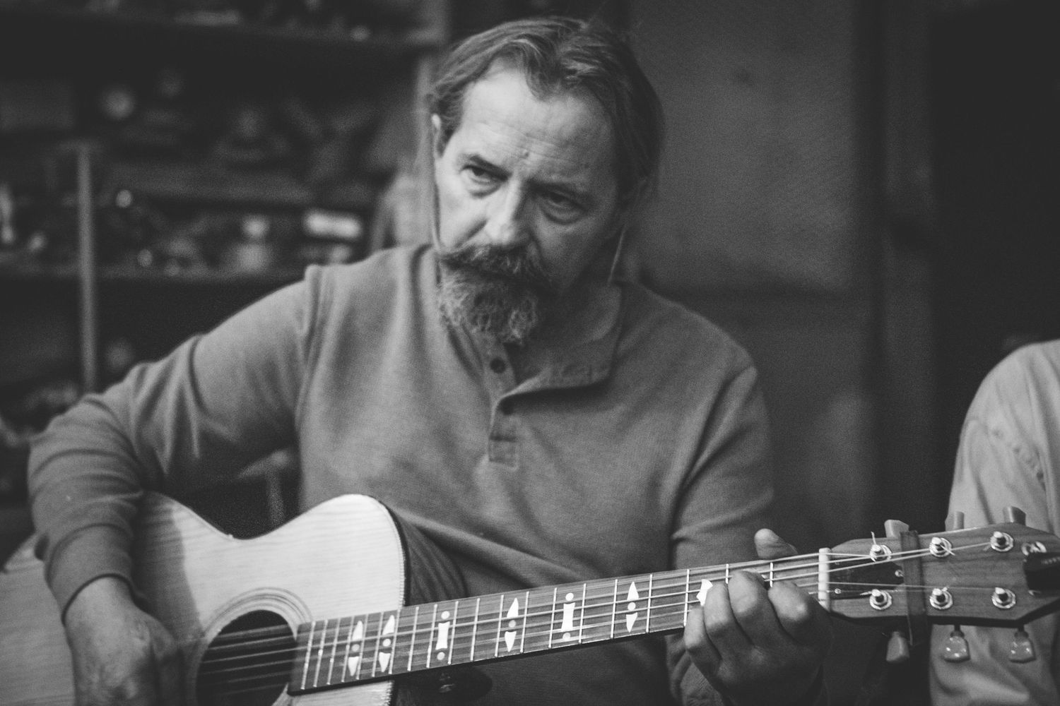 Bearded man playing acoustic guitar indoors captured in black and white portrait photography.