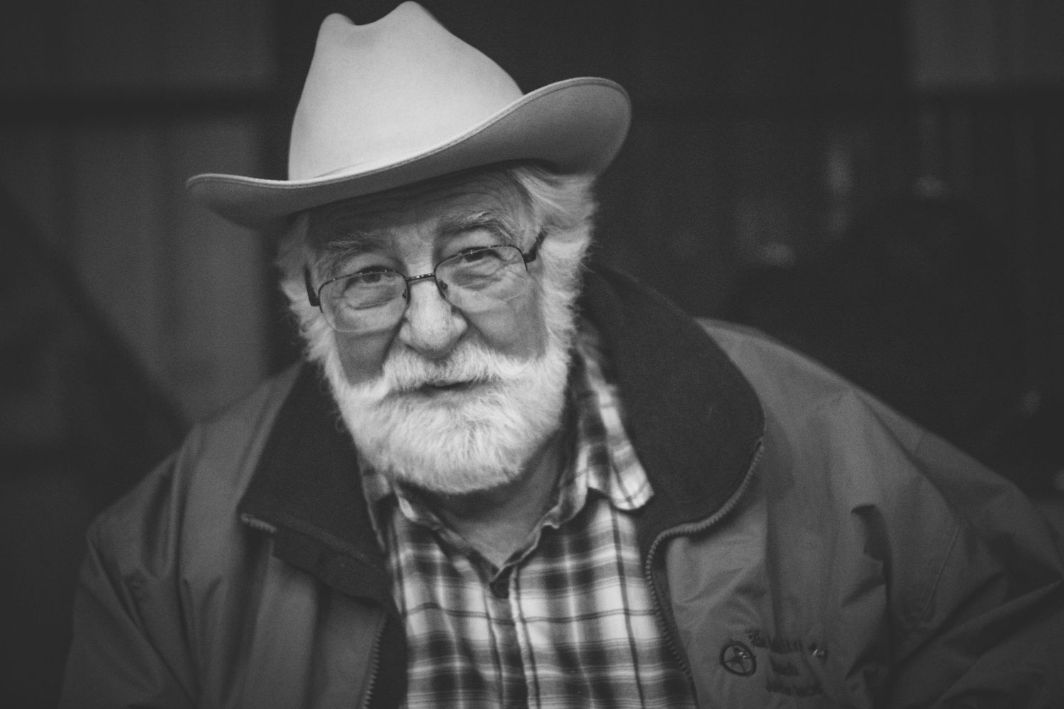 Portrait of bearded elderly man wearing white cowboy hat and glasses in black and white photography.