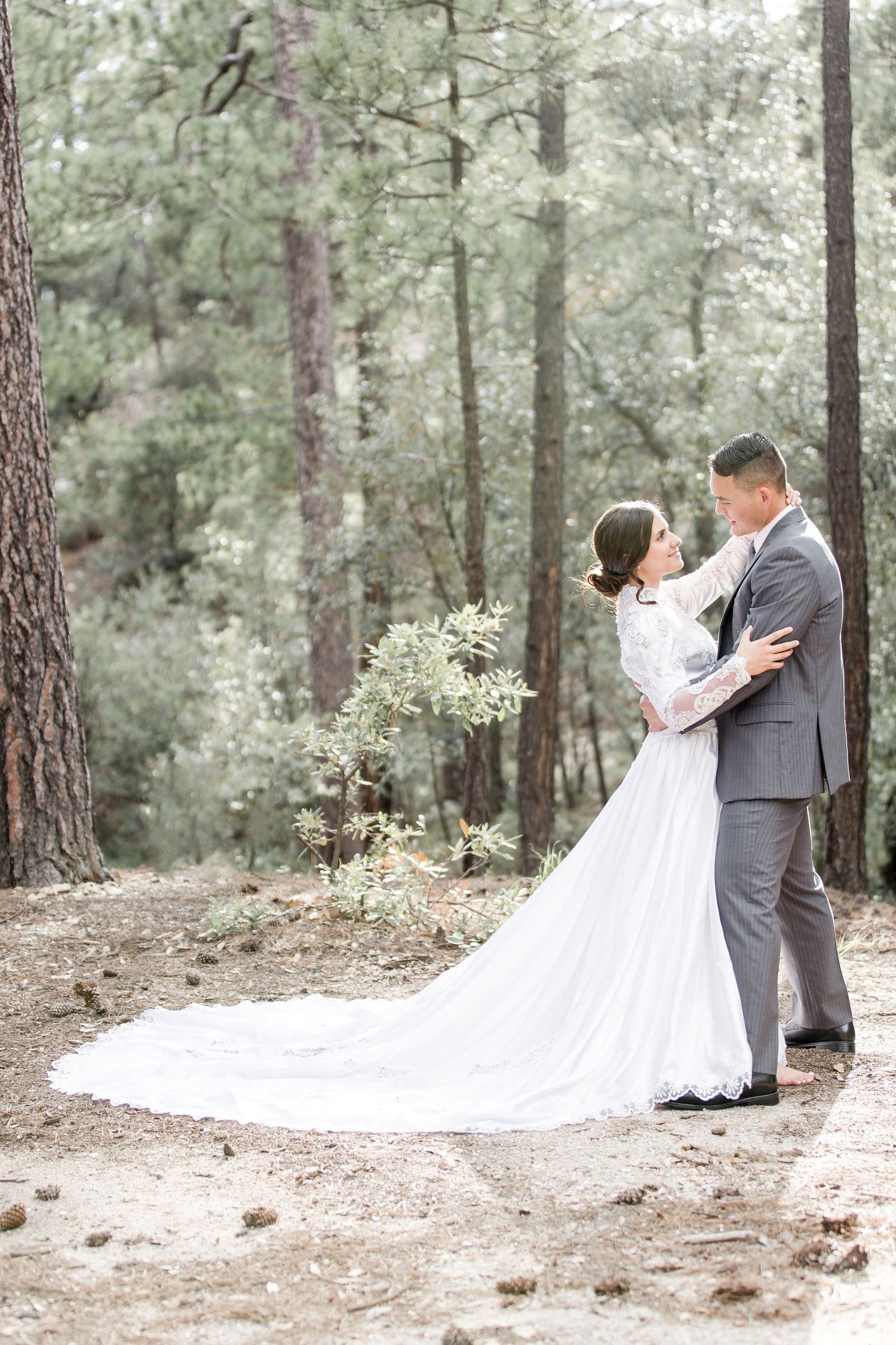 Elegant bride and groom embracing in a serene forest setting during their outdoor wedding ceremony.