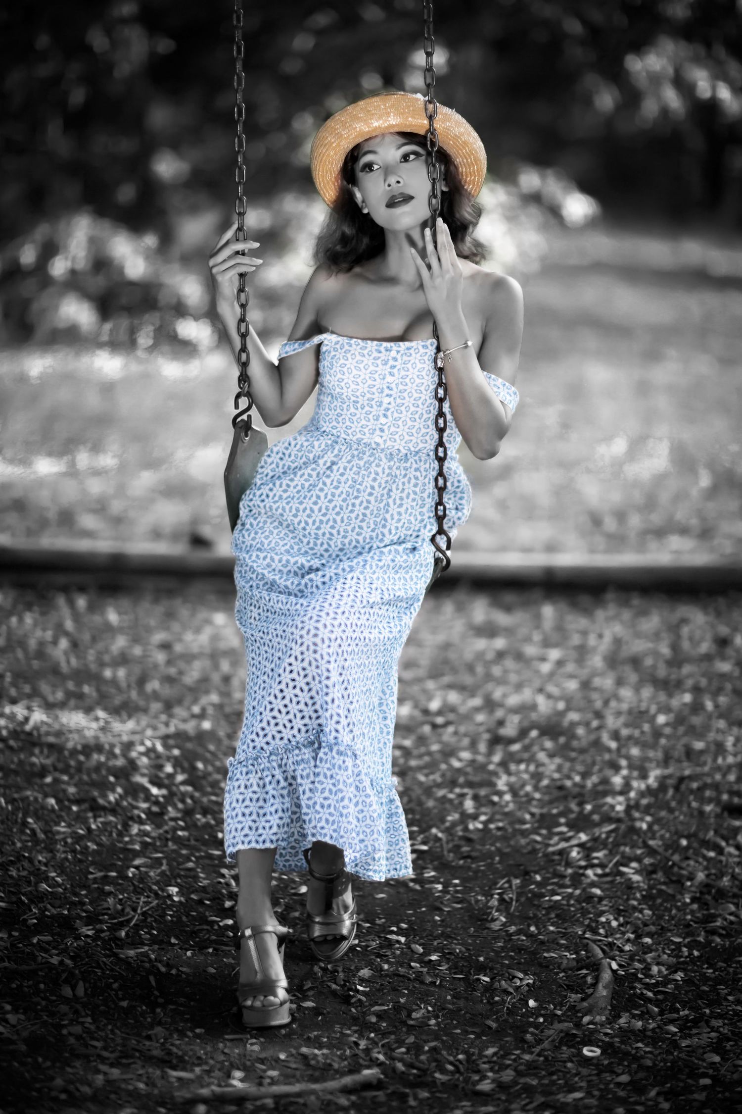 Woman in white dress and straw hat sitting on a swing in a black and white portrait.