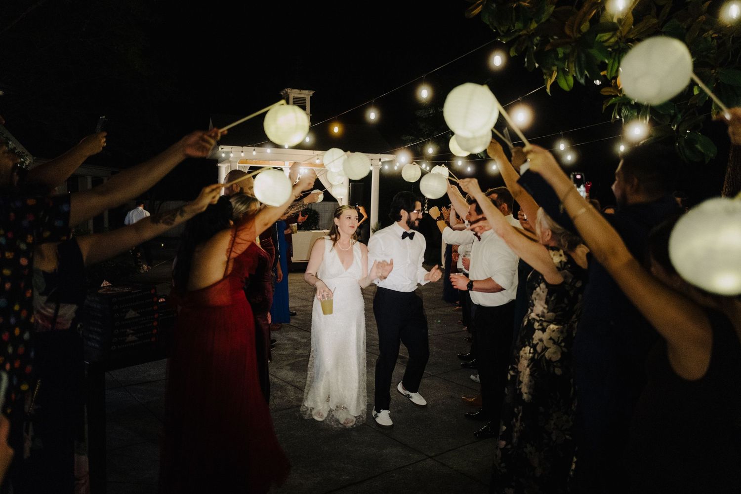 Wedding guests celebrate under glowing paper lanterns during an evening outdoor reception.