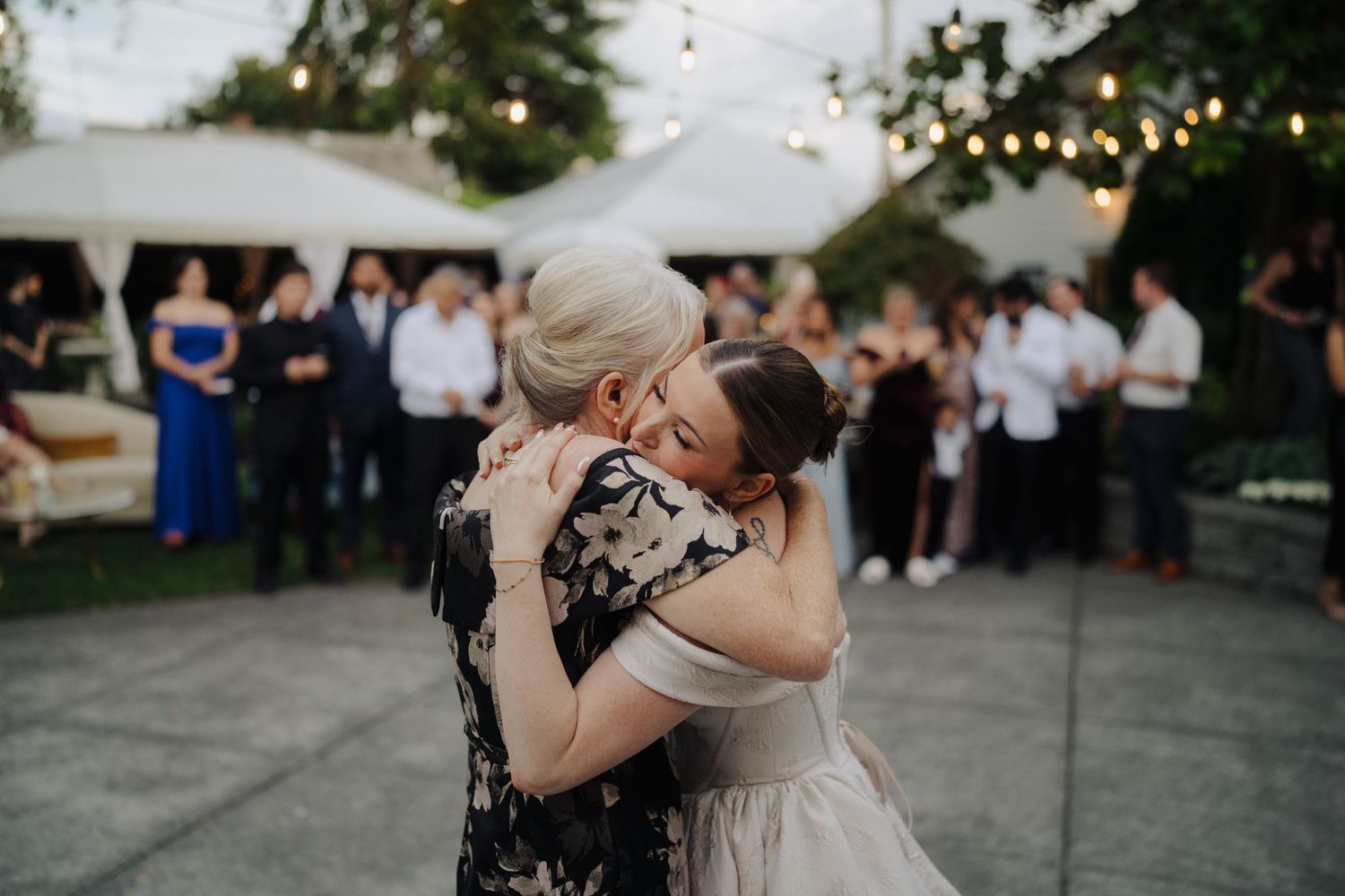 Emotional dance moment at outdoor wedding reception with guests watching under string lights.