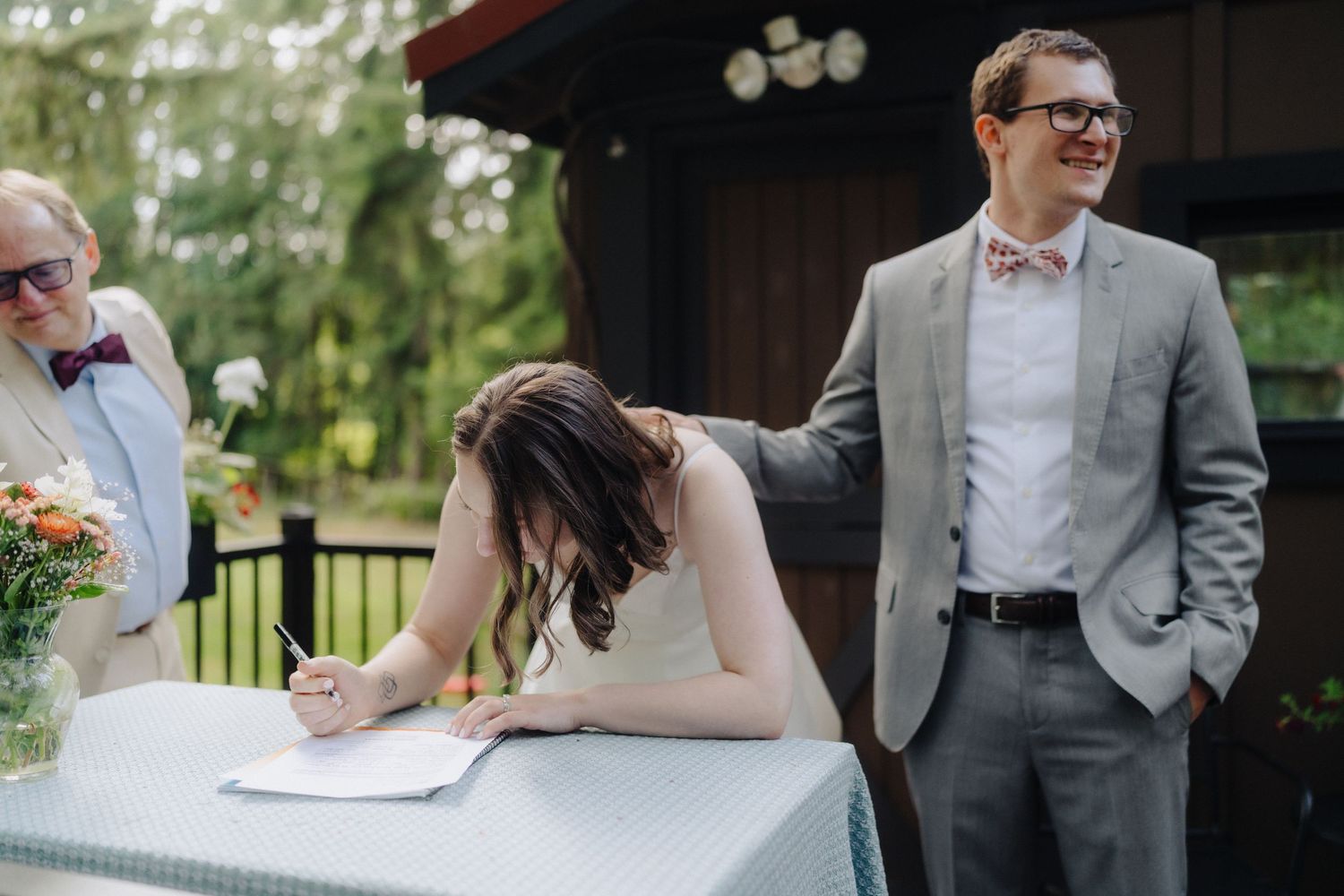 Wedding ceremony signing at a rustic outdoor venue with guests looking on.