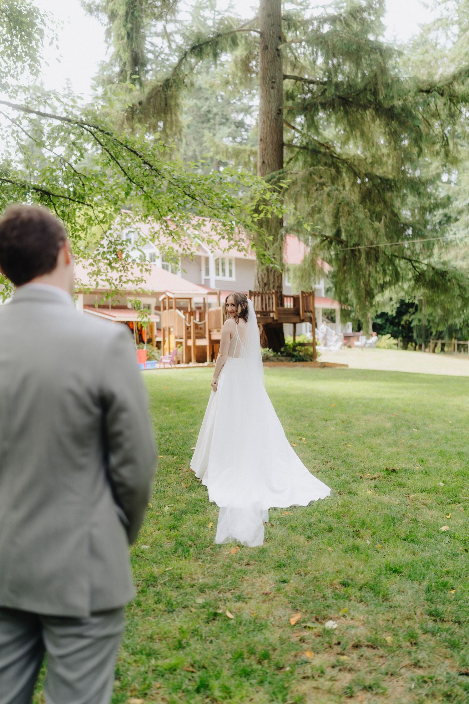 A romantic first look sequence unfolds on a grassy lawn with evergreen trees in the background.