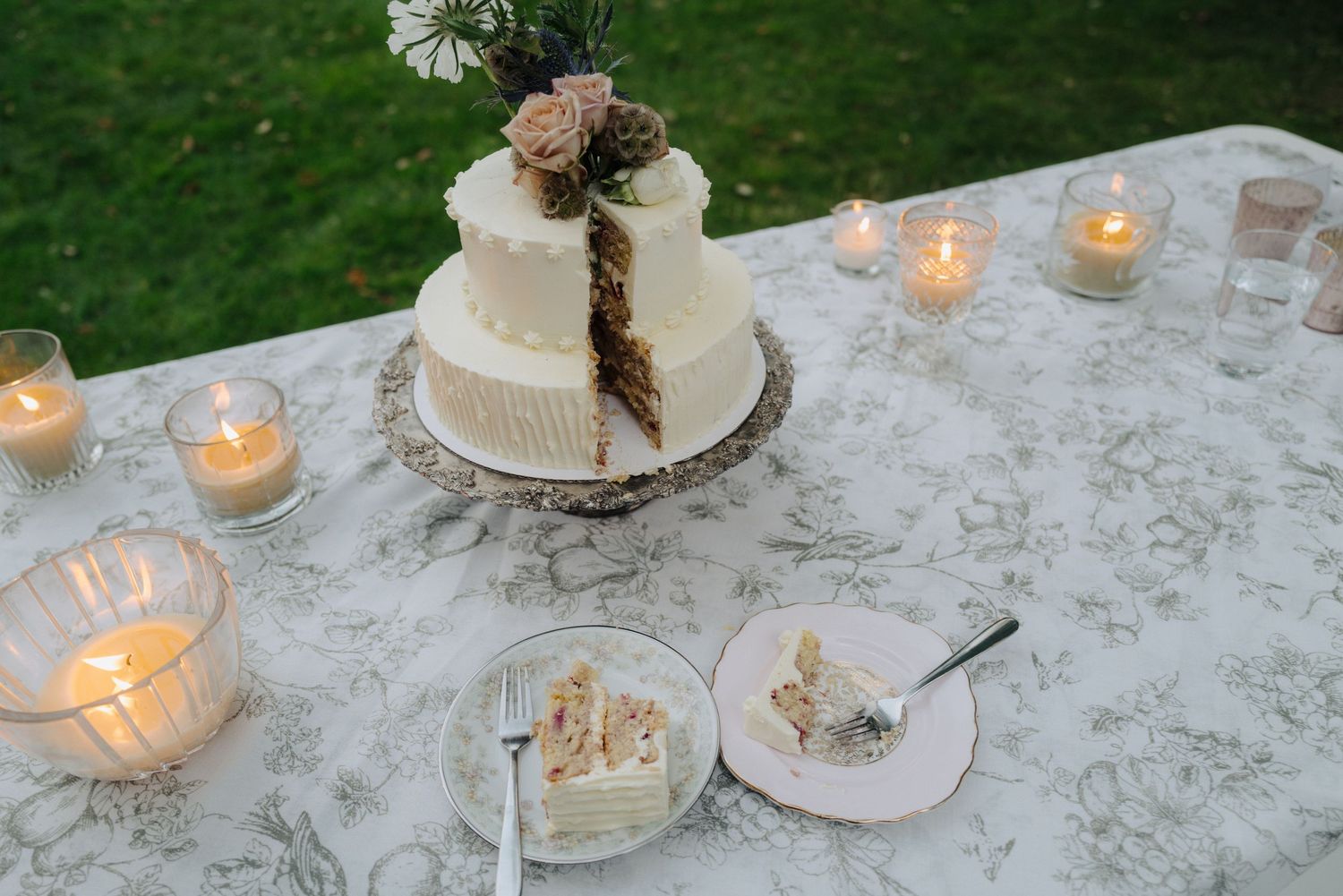 A white wedding cake with floral decorations surrounded by glowing candles on a lace tablecloth.
