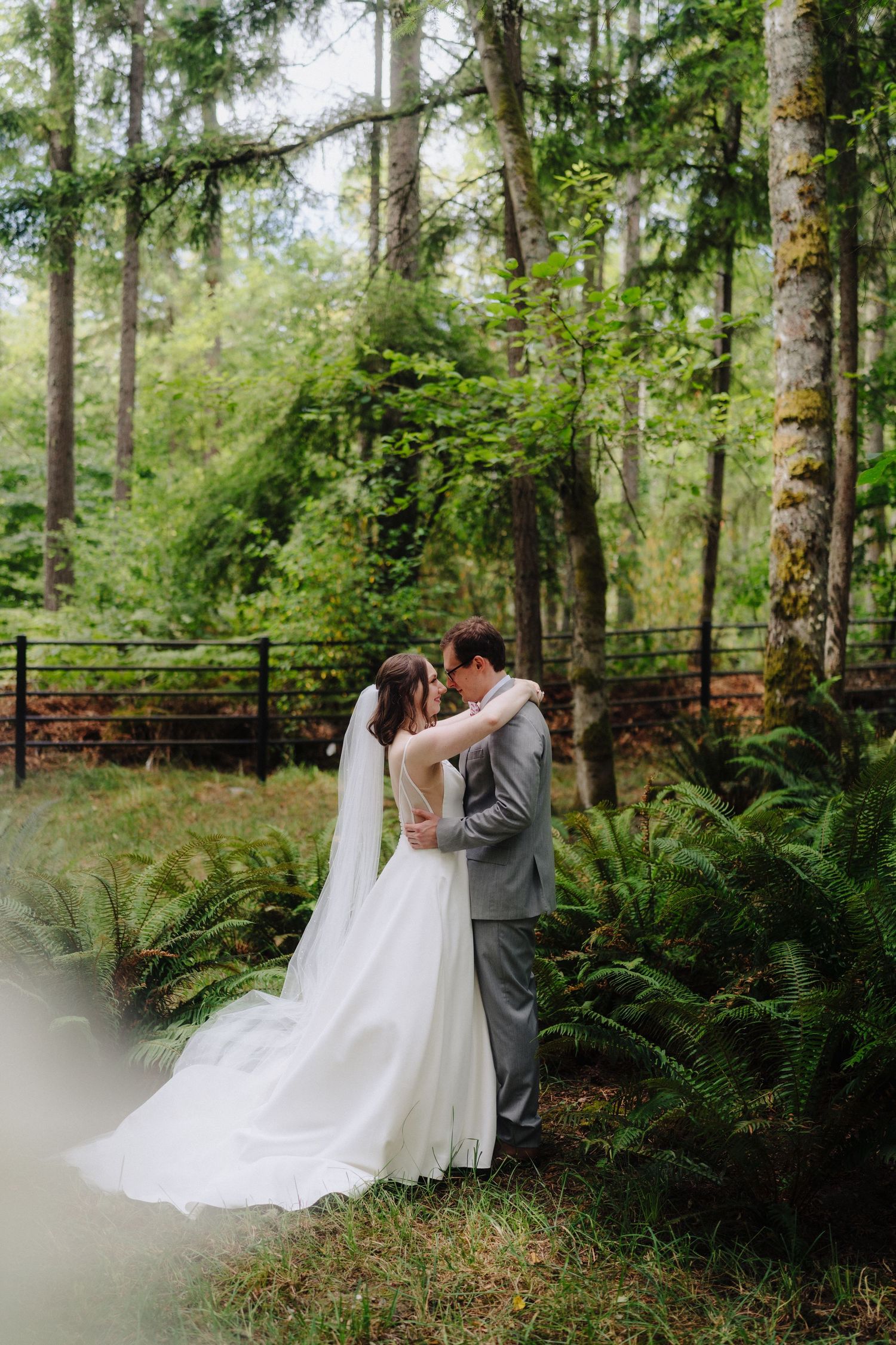 A romantic wedding couple shares intimate moments in a lush forest setting with ferns and tall trees.