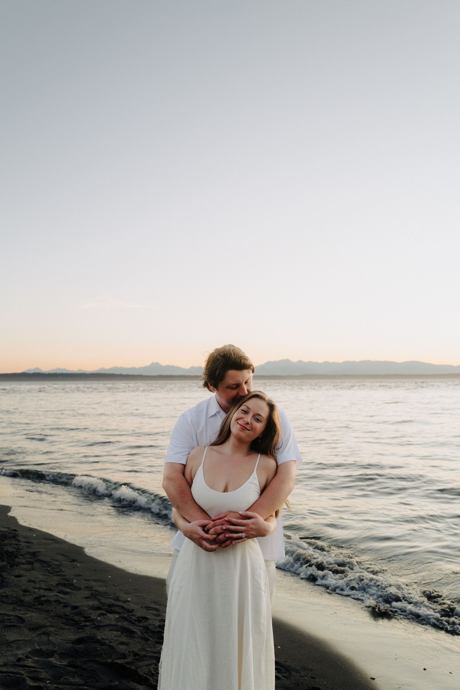 A couple sharing an intimate moment on the beach during sunset with waves gently rolling in.