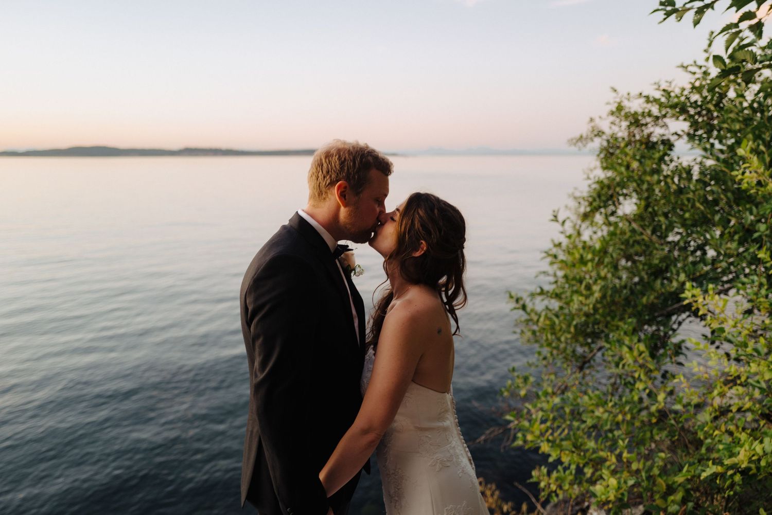 Romantic sunset wedding portraits overlooking a serene lake with lush greenery in the foreground.