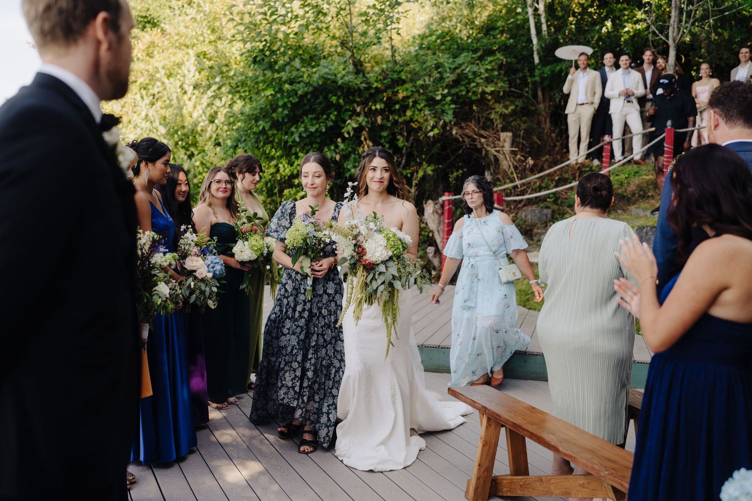 Wedding guests gathered on a wooden deck for an outdoor ceremony under trees.