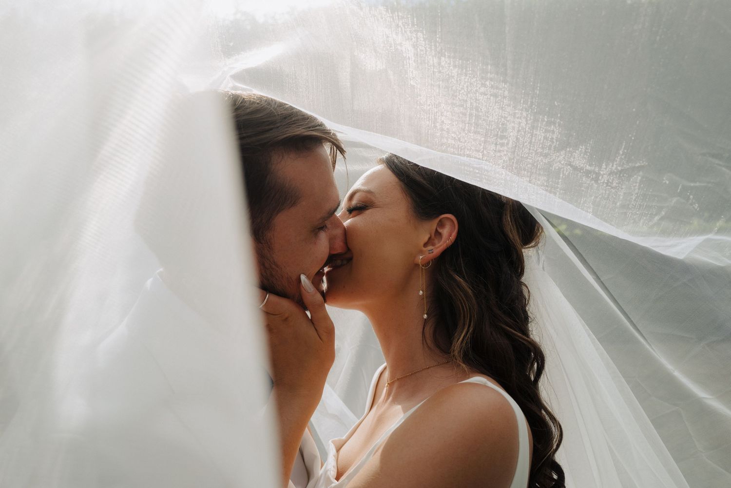 A romantic moment captured through delicate white tulle veil in soft lighting.