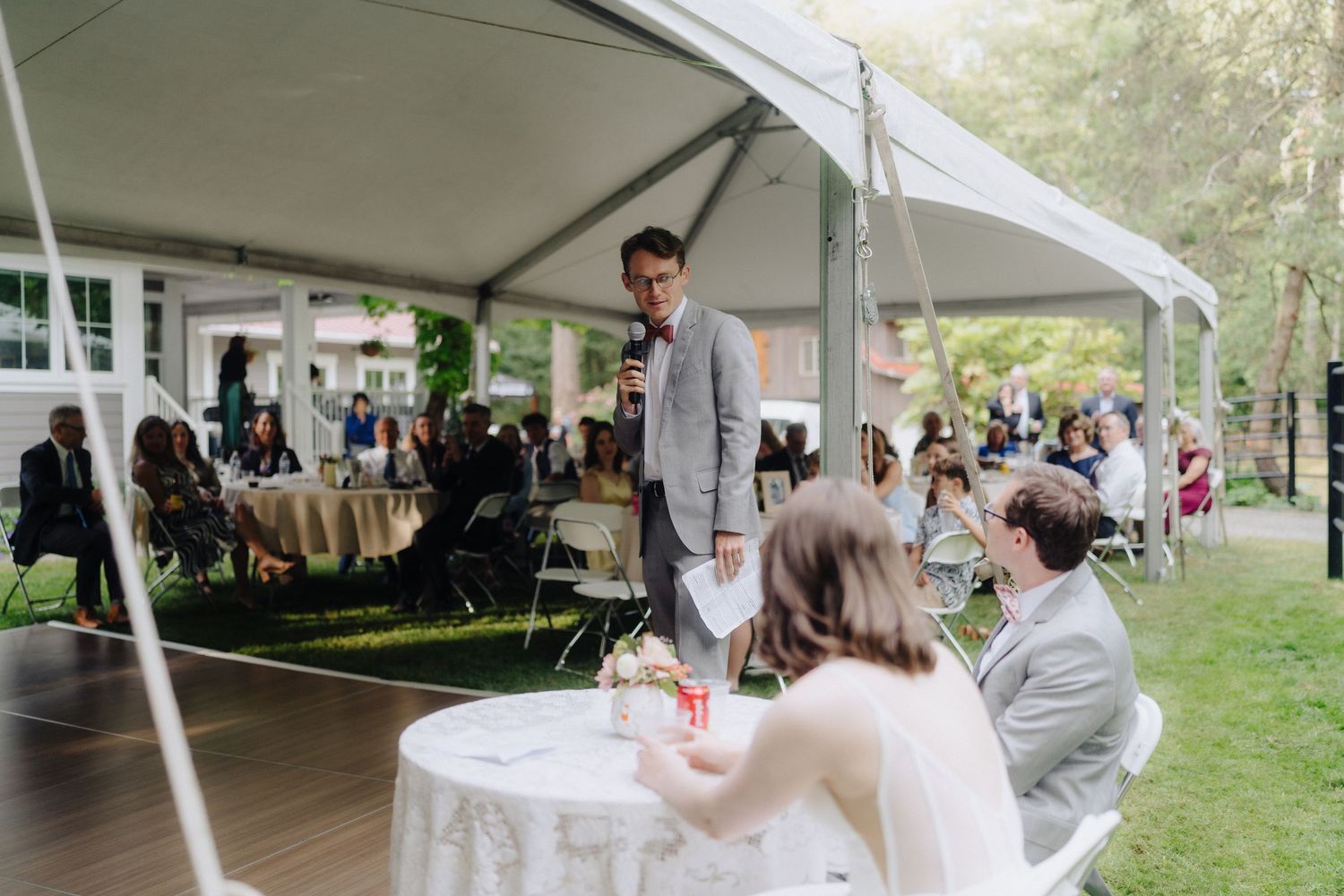 Wedding reception setup under white tents in a forest clearing.