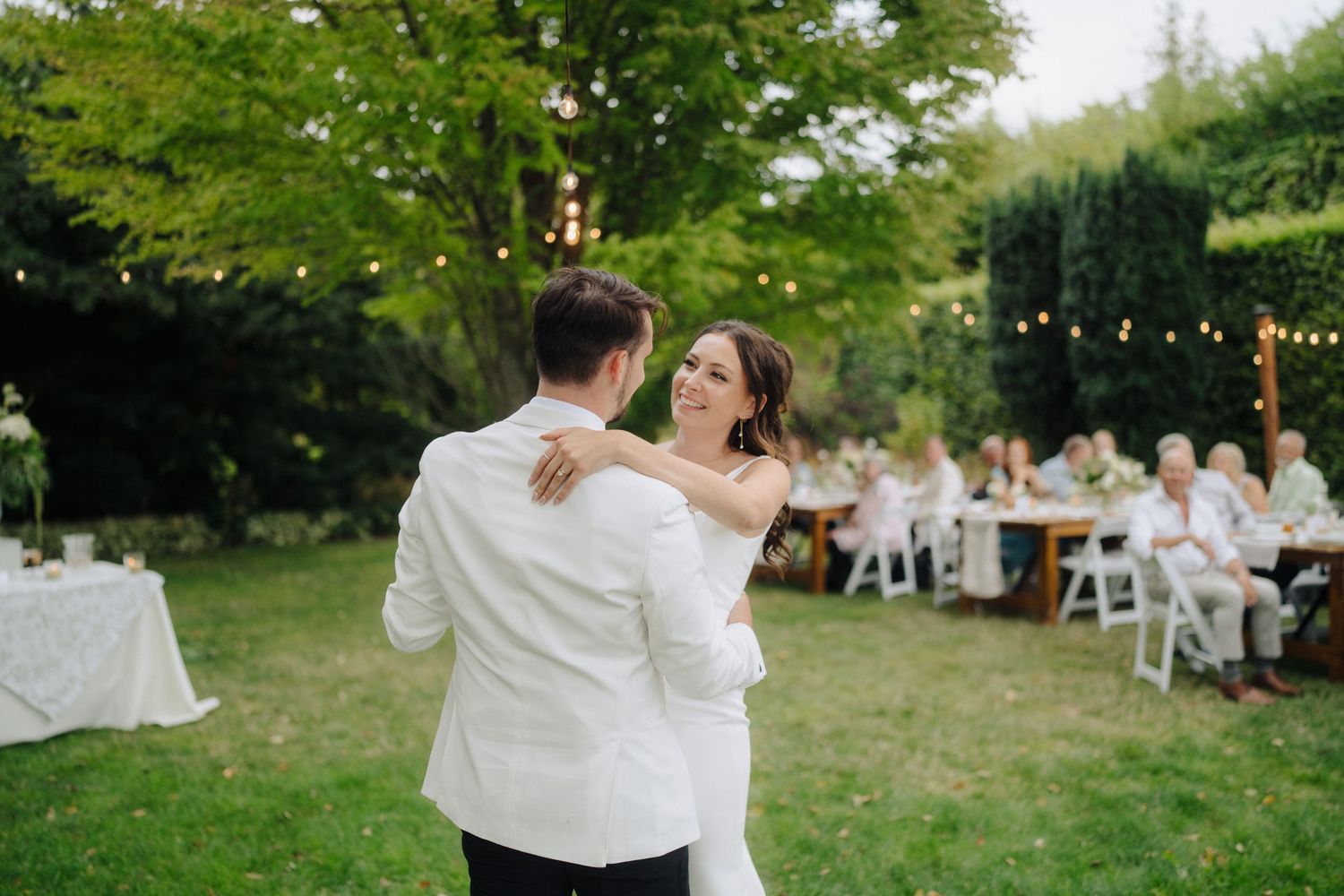 Wedding celebration in a green garden setting with tables and dancing guests.