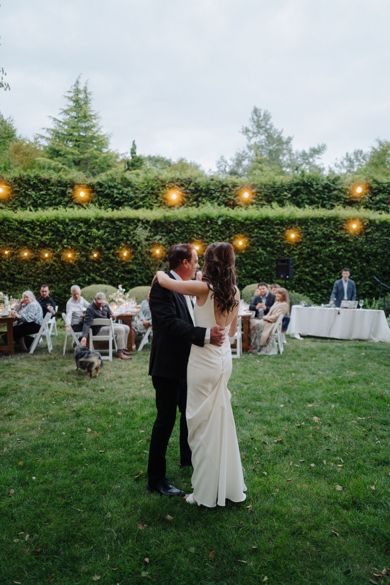 Couples slow dancing on grass under string lights at outdoor wedding reception.