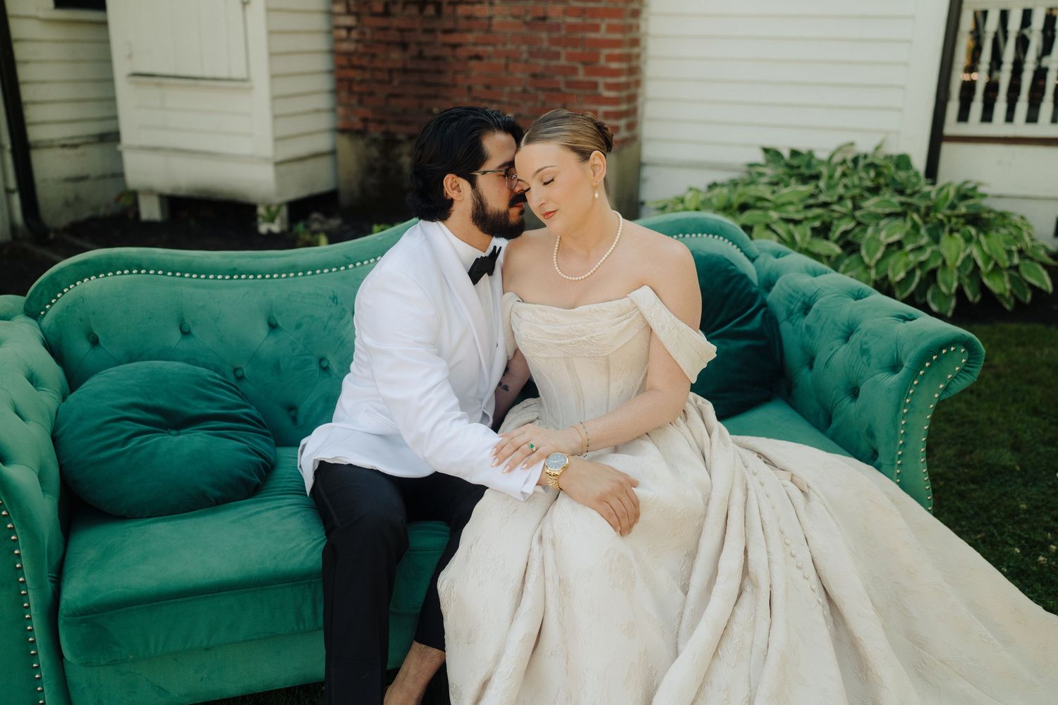 Couple shares romantic moments on an elegant emerald green velvet couch during their wedding day.