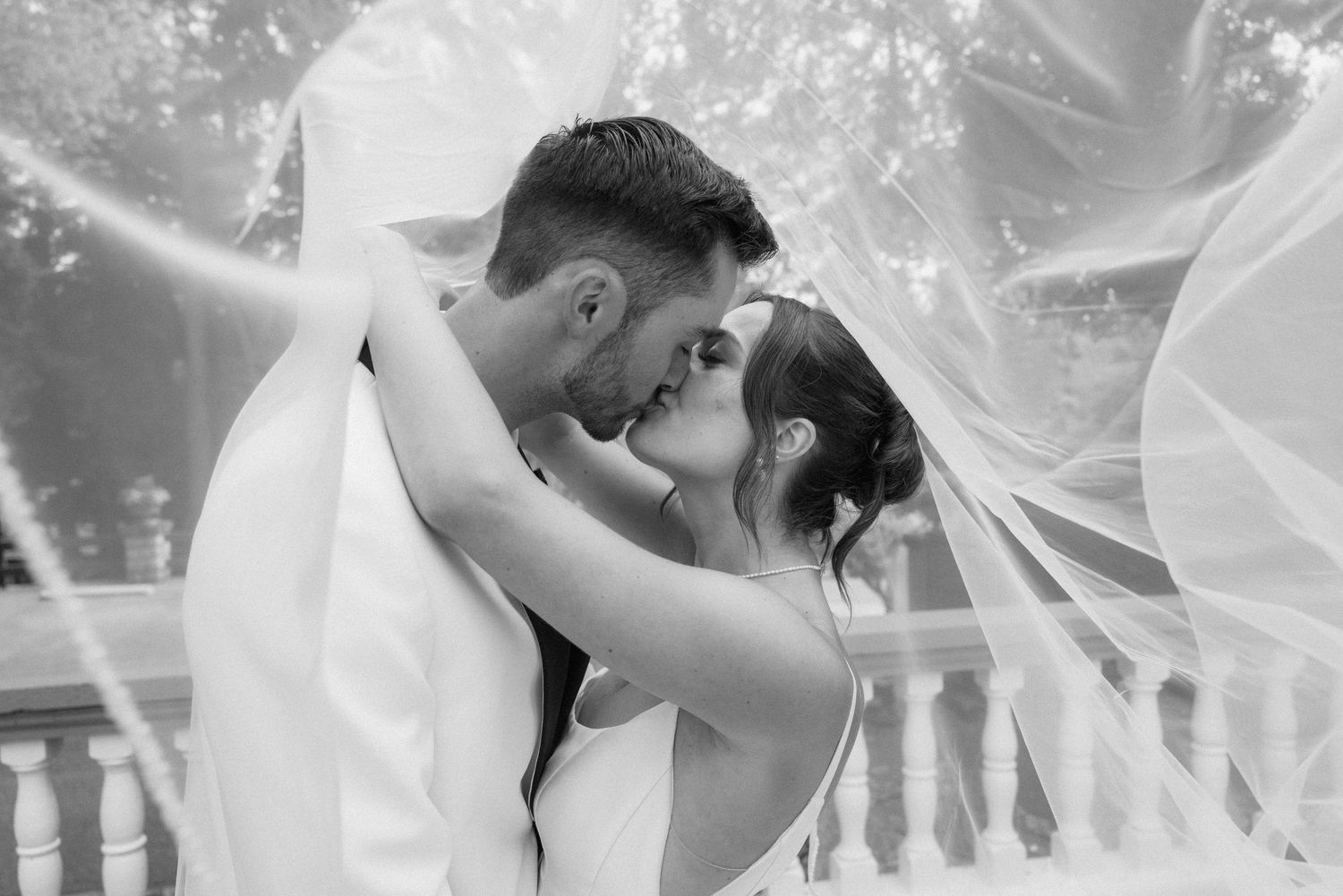 A romantic black and white portrait of a couple sharing an intimate moment under a flowing veil.