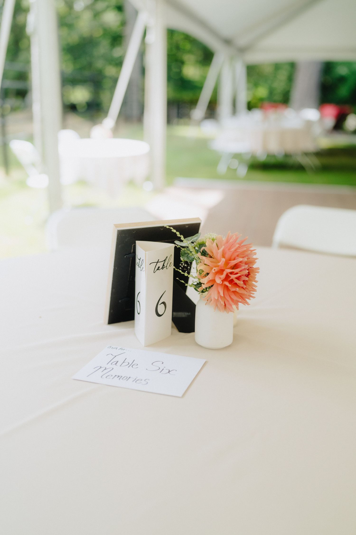 Wedding reception table details with coral flowers and name cards on white linens.