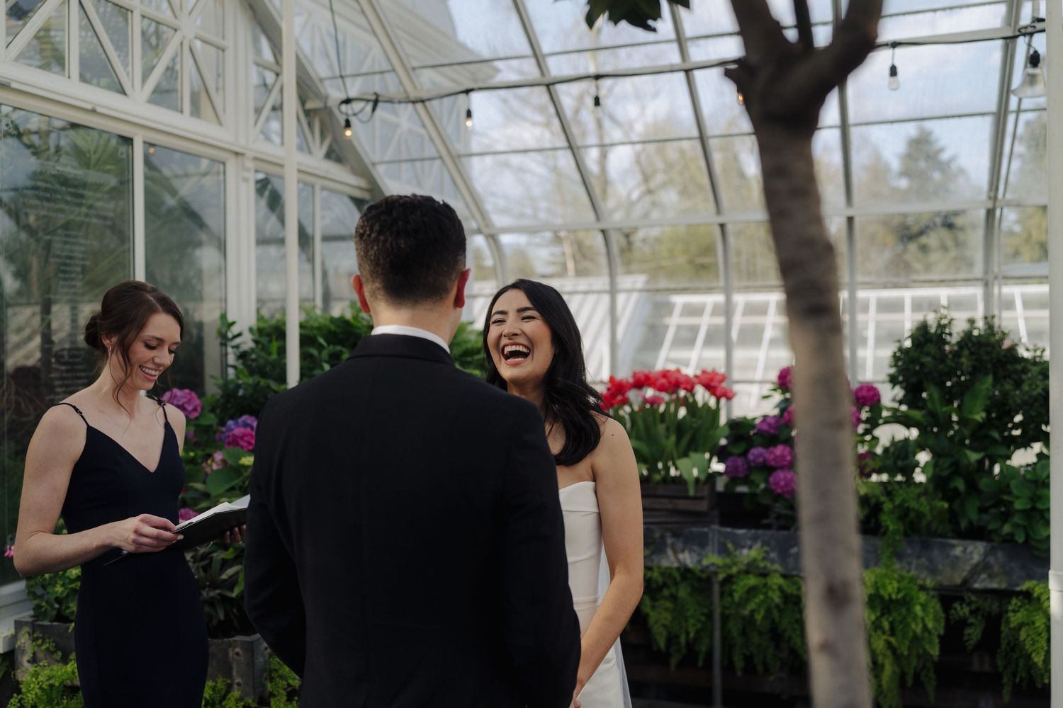 A joyful wedding ceremony moment captured inside a bright greenhouse with glass ceiling.