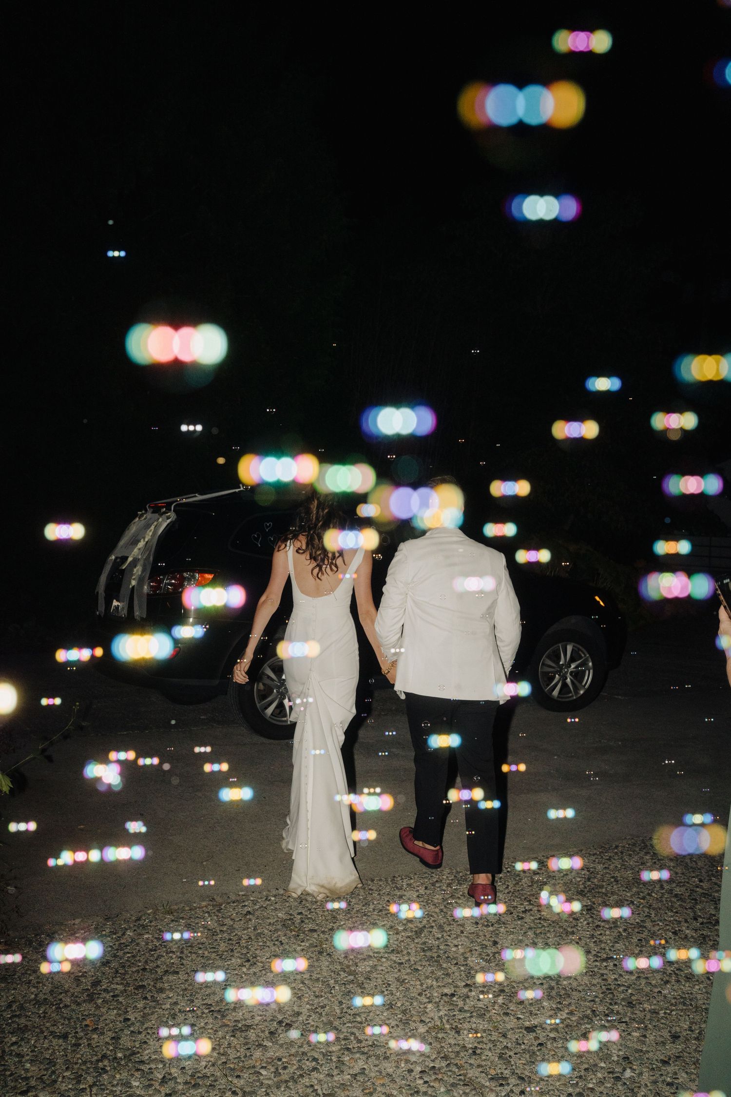 Couple walking at night surrounded by colorful bokeh lights on the ground.