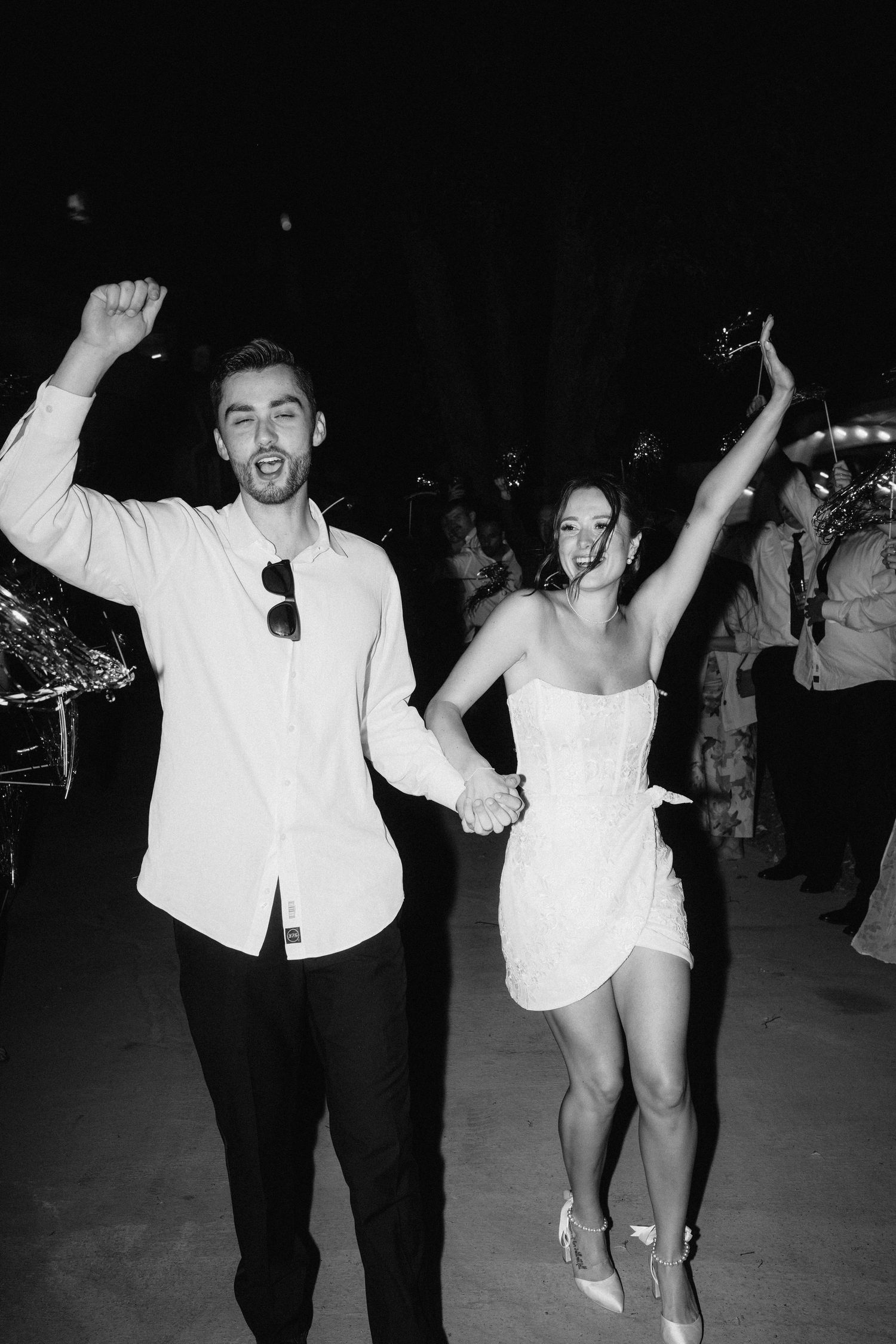 People dancing energetically at a nighttime wedding reception with arms raised in celebration.