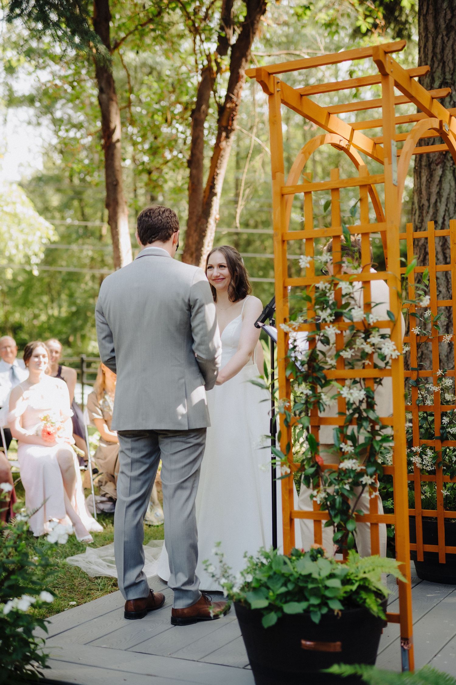 Wedding ceremony setup with wooden pergola and floral decorations in an outdoor garden setting.