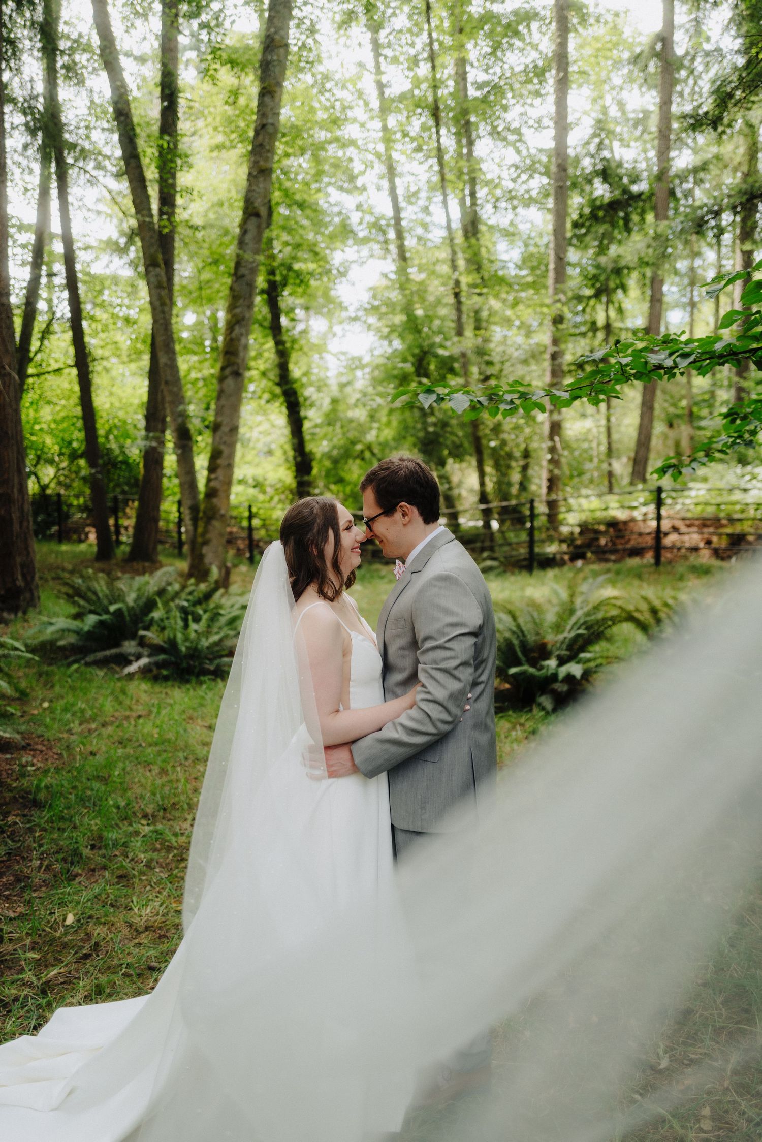 Flowing white wedding dress creates dramatic effect against lush forest greenery.