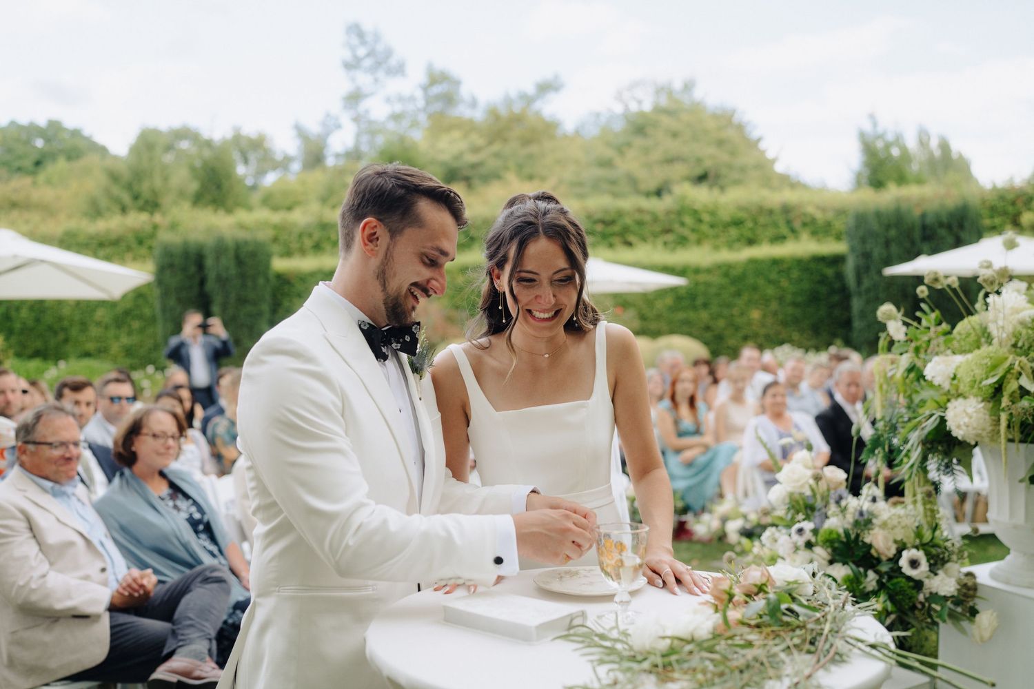Wedding reception table settings with white linens and floral centerpieces outdoors.