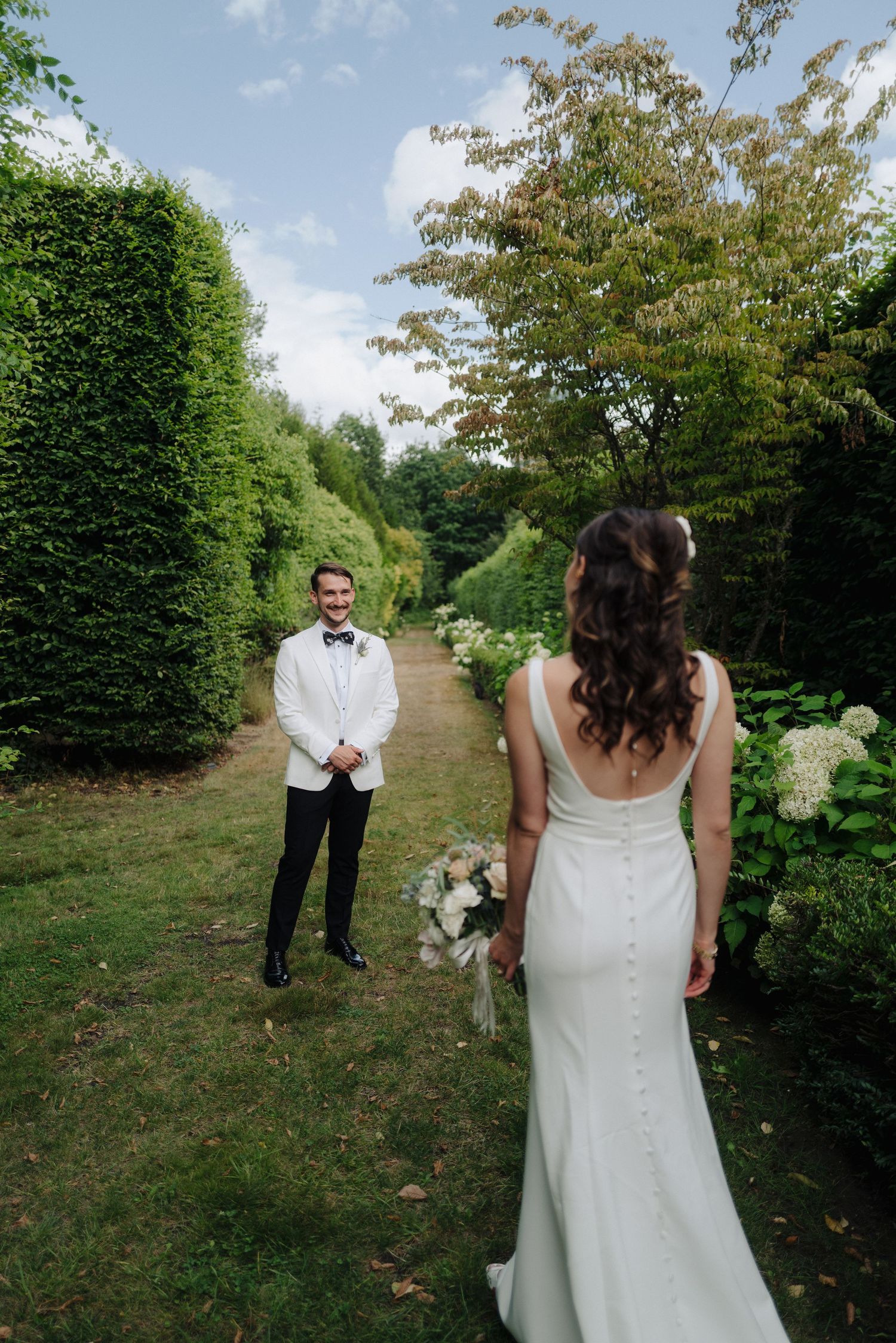 An outdoor wedding scene with tall hedges and trees creating a natural garden pathway.