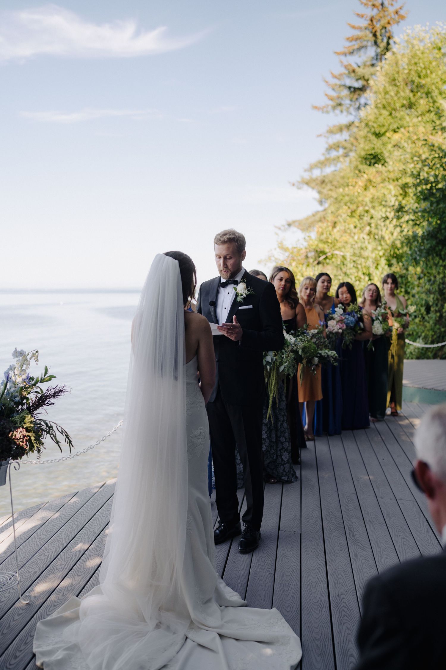 Wedding ceremony on a wooden deck with scenic ocean views and evergreen trees in the background.