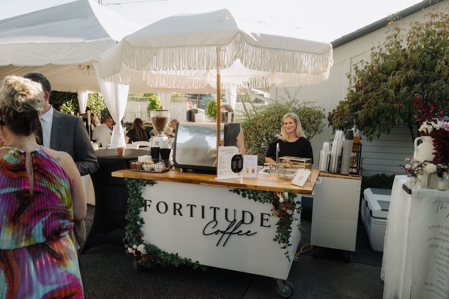 A rustic outdoor bar setup with white tent and 'Fortitude' signage.