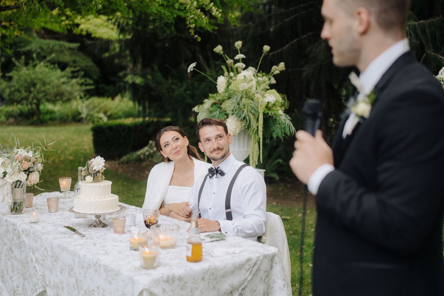 Wedding party seated at an elegant outdoor reception table with white decor.