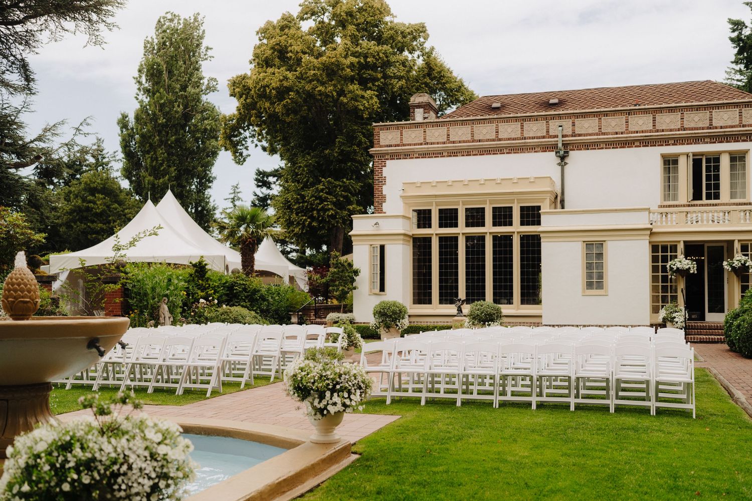 Elegant outdoor wedding venue setup with white chairs and lush gardens for a ceremony.