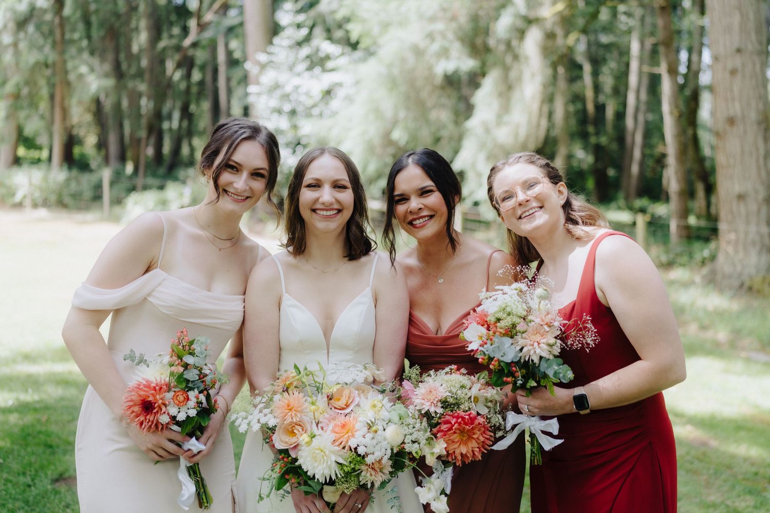 Wedding party in burgundy and neutral dresses holding bouquets in outdoor setting.