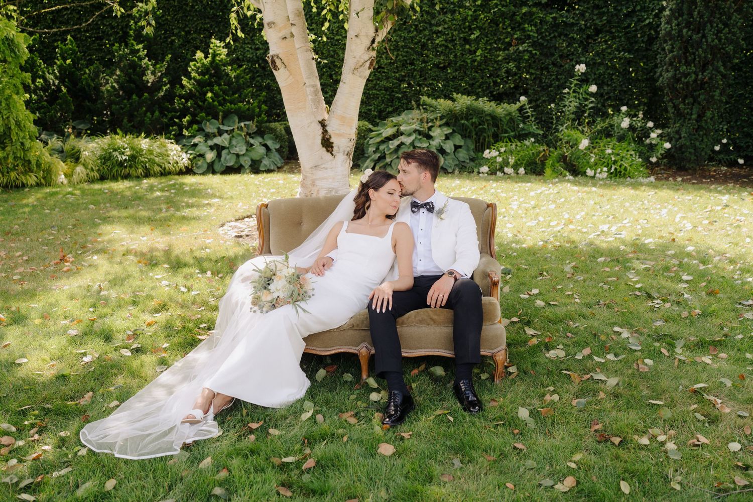 Wedding couple and guests relaxing on wooden benches in a garden setting.