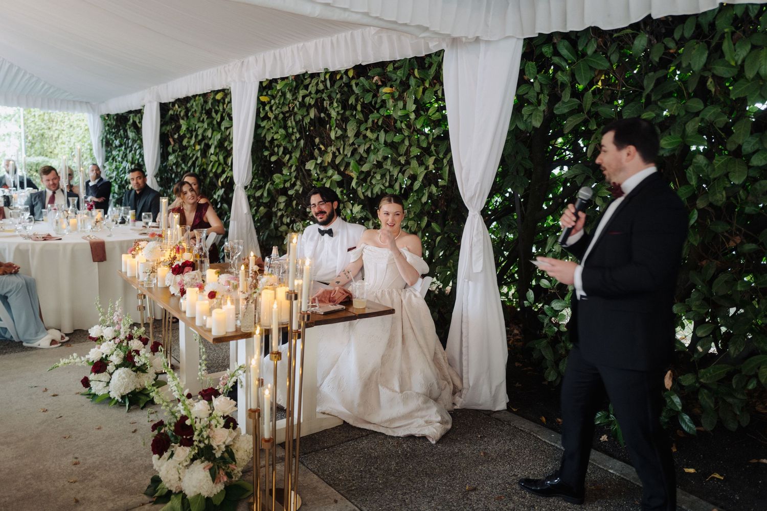 Indoor-outdoor wedding reception space with white tent draping and natural greenery walls.