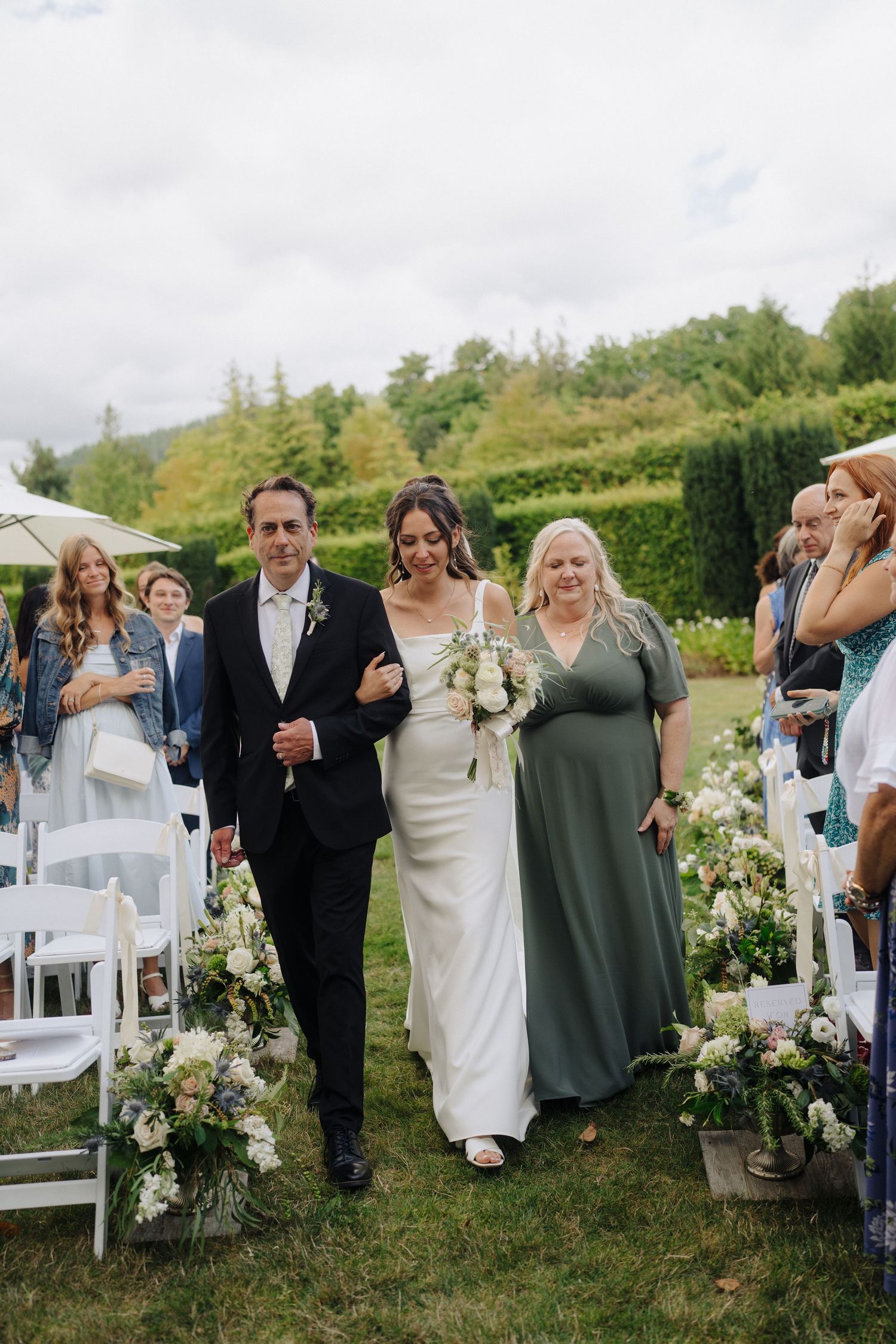 Wedding guests seated in white chairs for an outdoor garden ceremony with floral decorations.